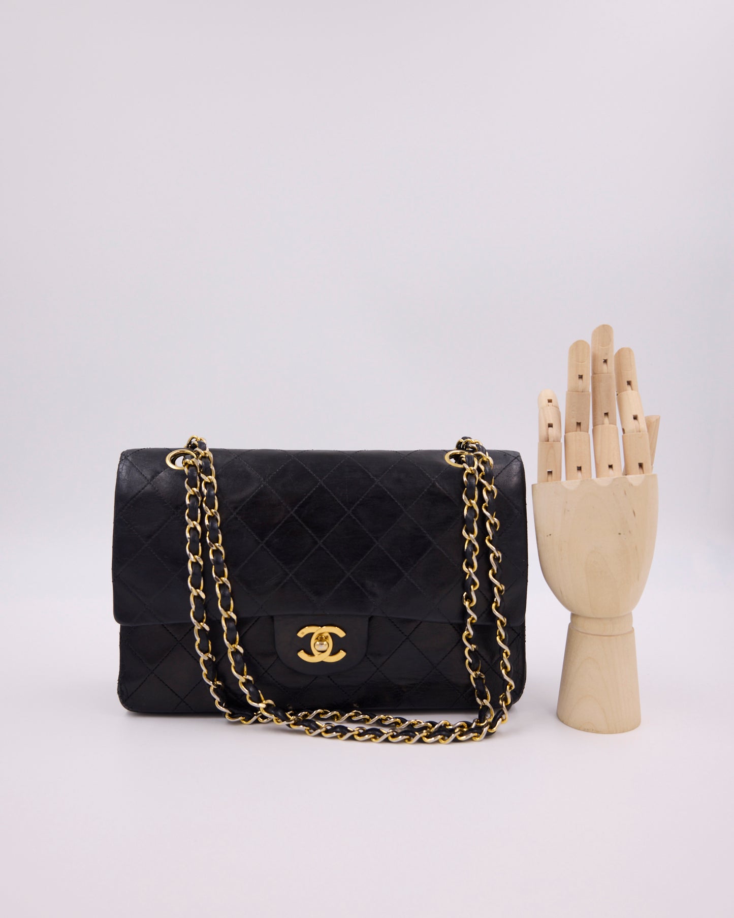 Schwarze gesteppte CHANEL-Handtasche mit goldener Kette neben einer hölzernen Handbüste