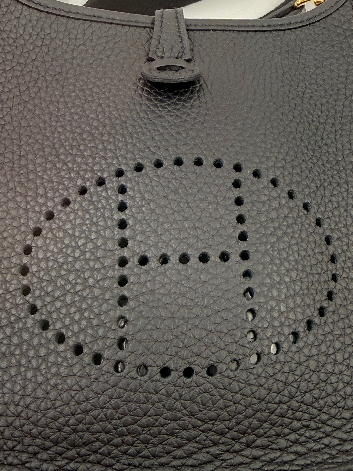 HERMÈS Evelyne 16 Taurillon Clemence schwarz GHW Detailansicht des perforierten H-Logos auf schwarzem genarbtem Leder.