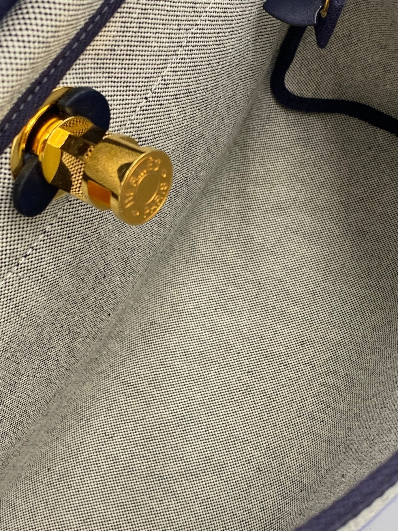 Nahaufnahme des goldenen Verschlusses der HERMES Herbag 31 Circuit auf grauem Canvas-Material mit marineblauen Lederdetails