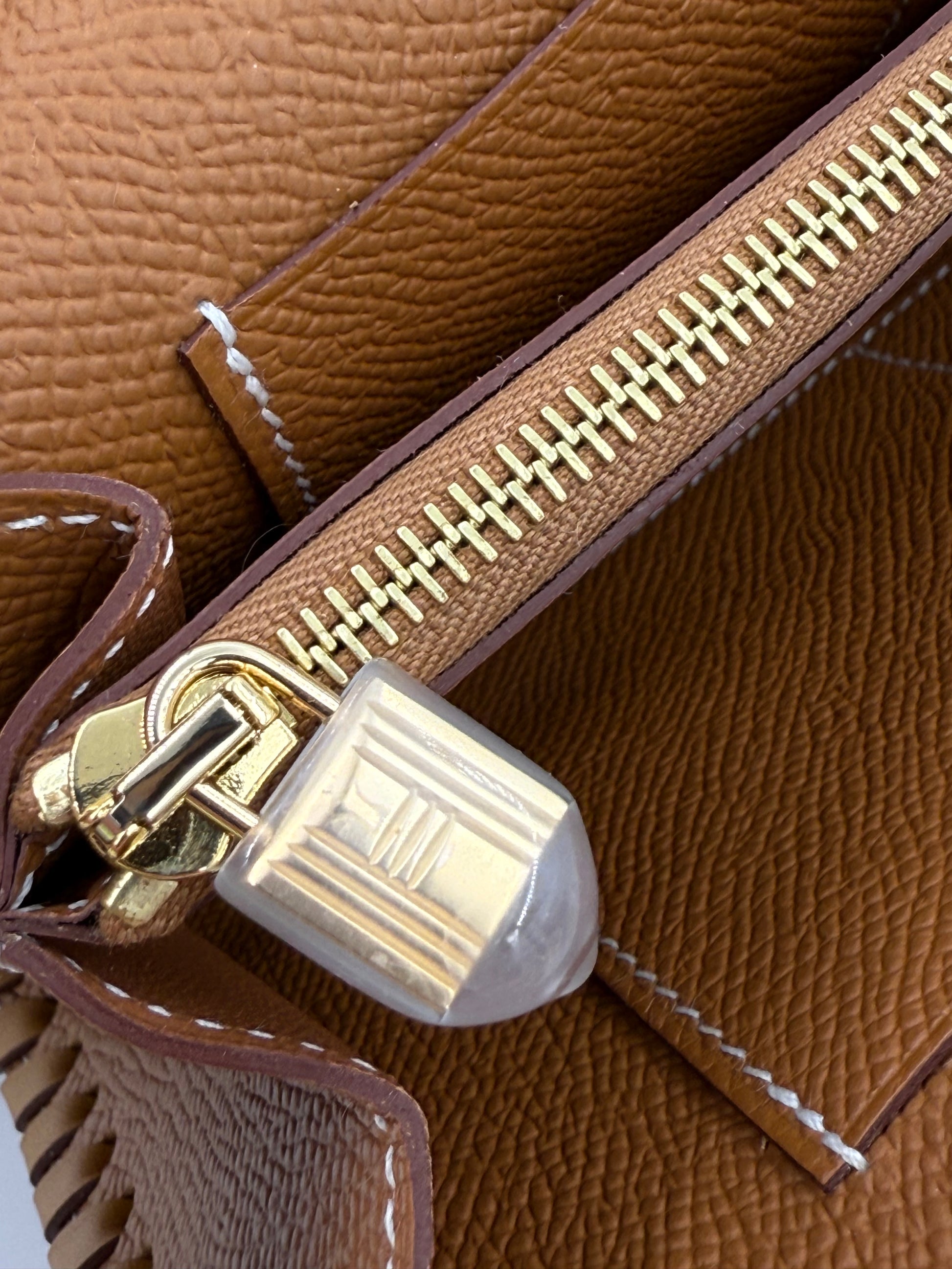 HERMÈS Kelly to Go Tressage Epsom Gold Detailaufnahme des goldenen Reißverschlusses und braunen Epsom-Leders.