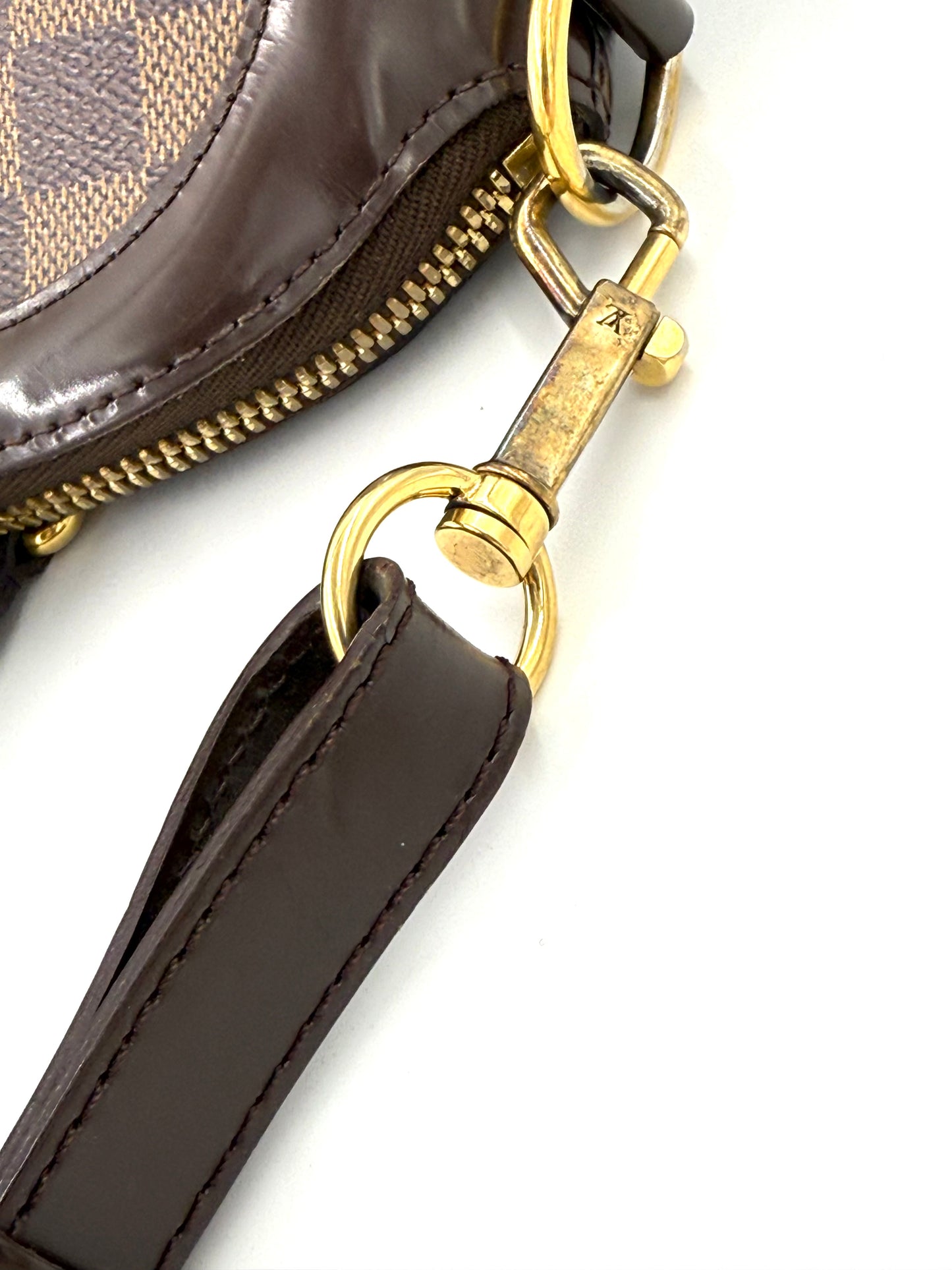 LOUIS VUITTON Trevi PM Damier Ebene Nahaufnahme des goldfarbenen Karabinerhakens und braunen Lederhenkels.