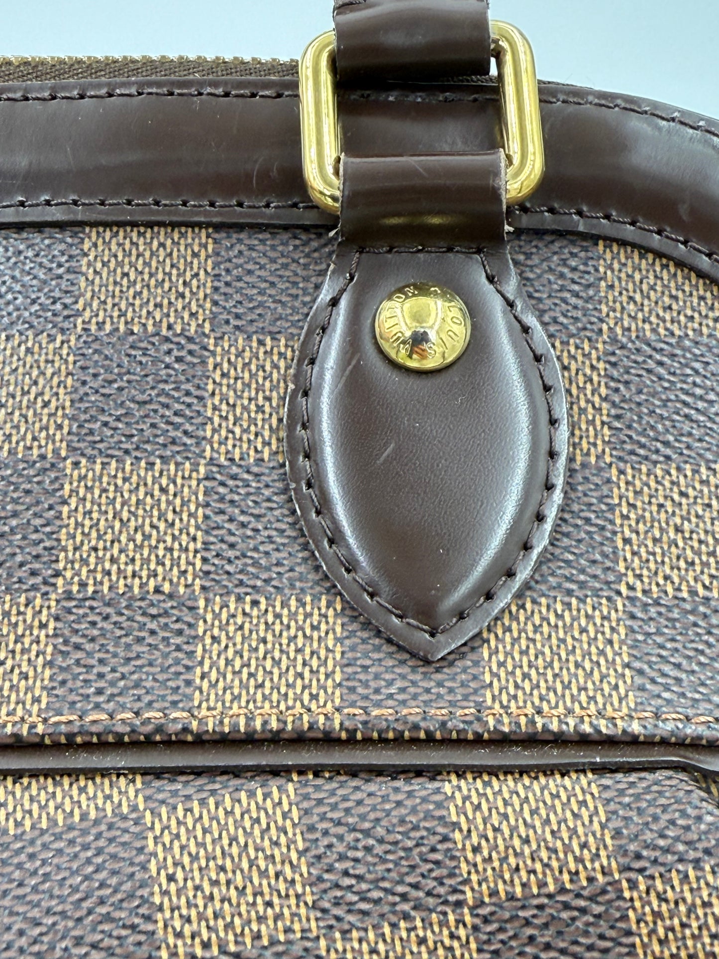LOUIS VUITTON Trevi PM Damier Ebene Nahaufnahme des Canvas-Musters mit Ledergriff und goldfarbenem Beschlag.