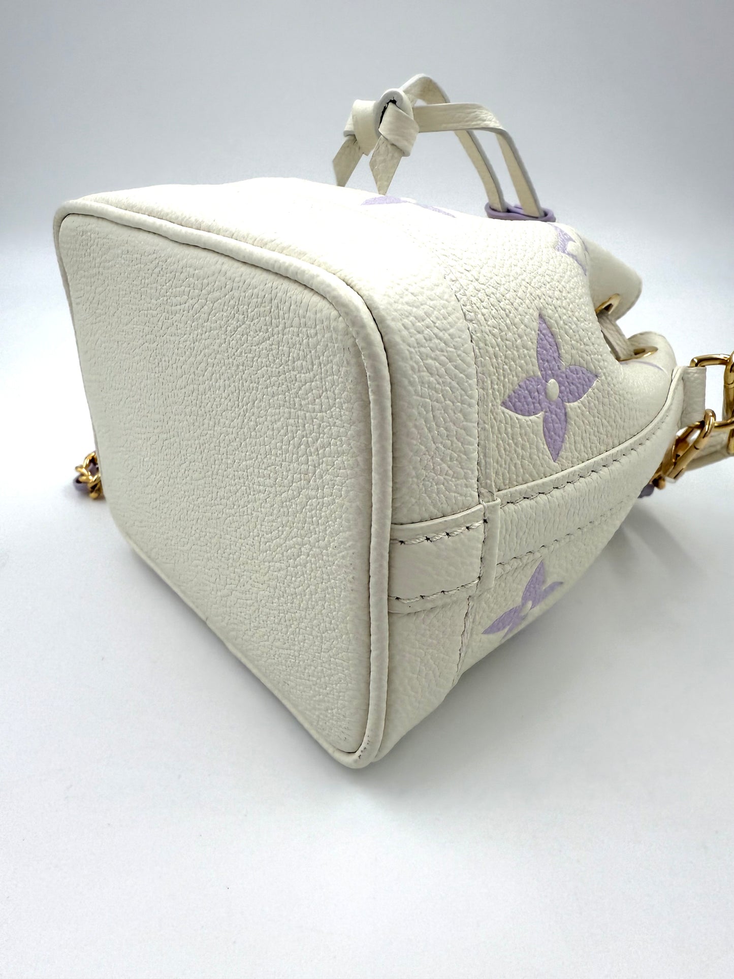 LOUIS VUITTON Nano Noe Monogram Empreinte Handtasche aus cremefarbenem Leder mit fliederfarbenen Monogramm-Motiven.