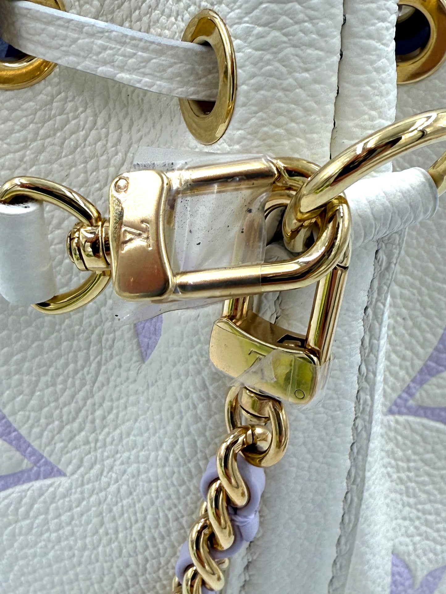 Nahaufnahme der goldfarbenen Metallbeschläge an der Louis Vuitton Nano Noe Monogram Empreinte in Creme und Flieder.