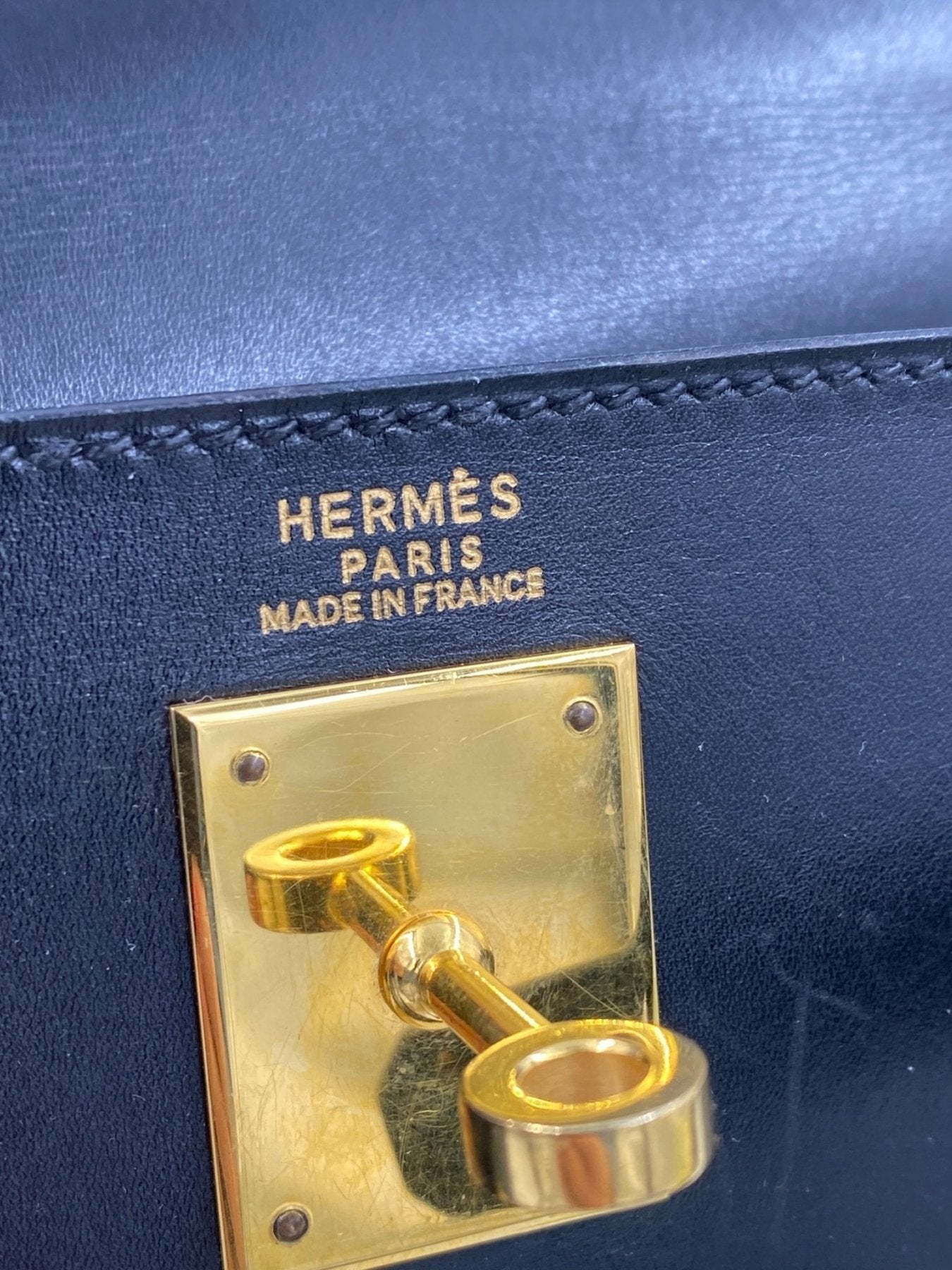 HERMES Kelly 32 Boxkalbsleder schwarz Detailaufnahme mit goldenem Drehverschluss und Markenpraegung auf schwarzem Leder