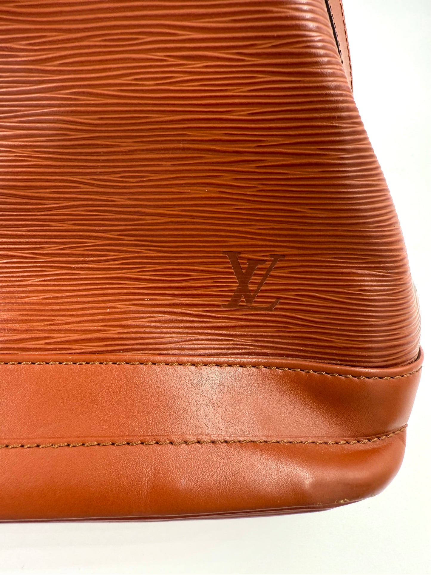 Nahaufnahme der braunen Louis Vuitton Noe Grande Epi Kenian Tasche mit geprägtem LV-Logo und glattem Lederboden.