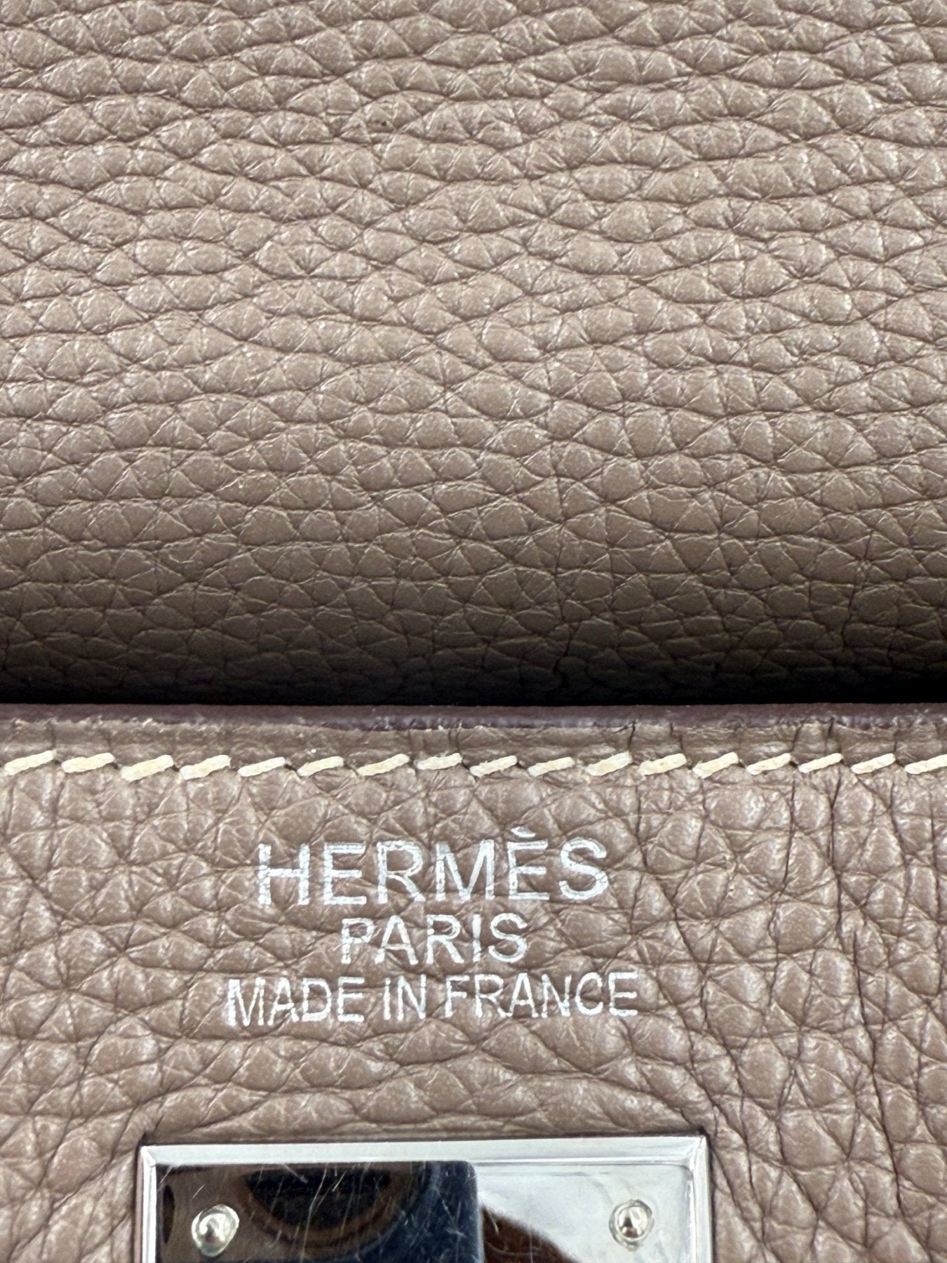 Nahaufnahme der Hermes Markierung auf einer Kelly 35 Tasche in Etoupe Leder mit charakteristischer Kornstruktur