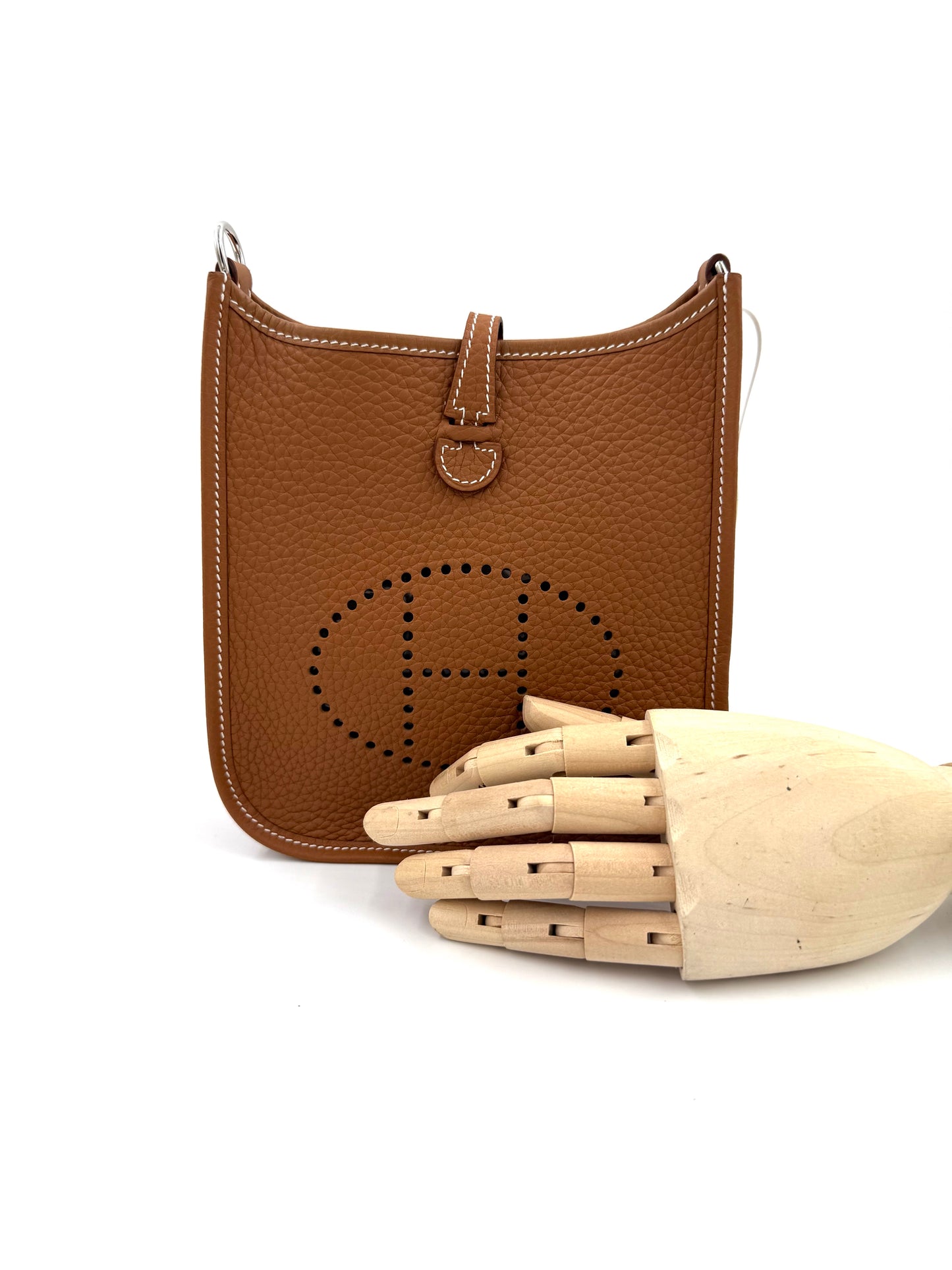 Braune HERMÈS Evelyne 16 gold PHW aus genarbtem Leder, präsentiert mit einem hölzernen Handmodell vor weißem Hintergrund.