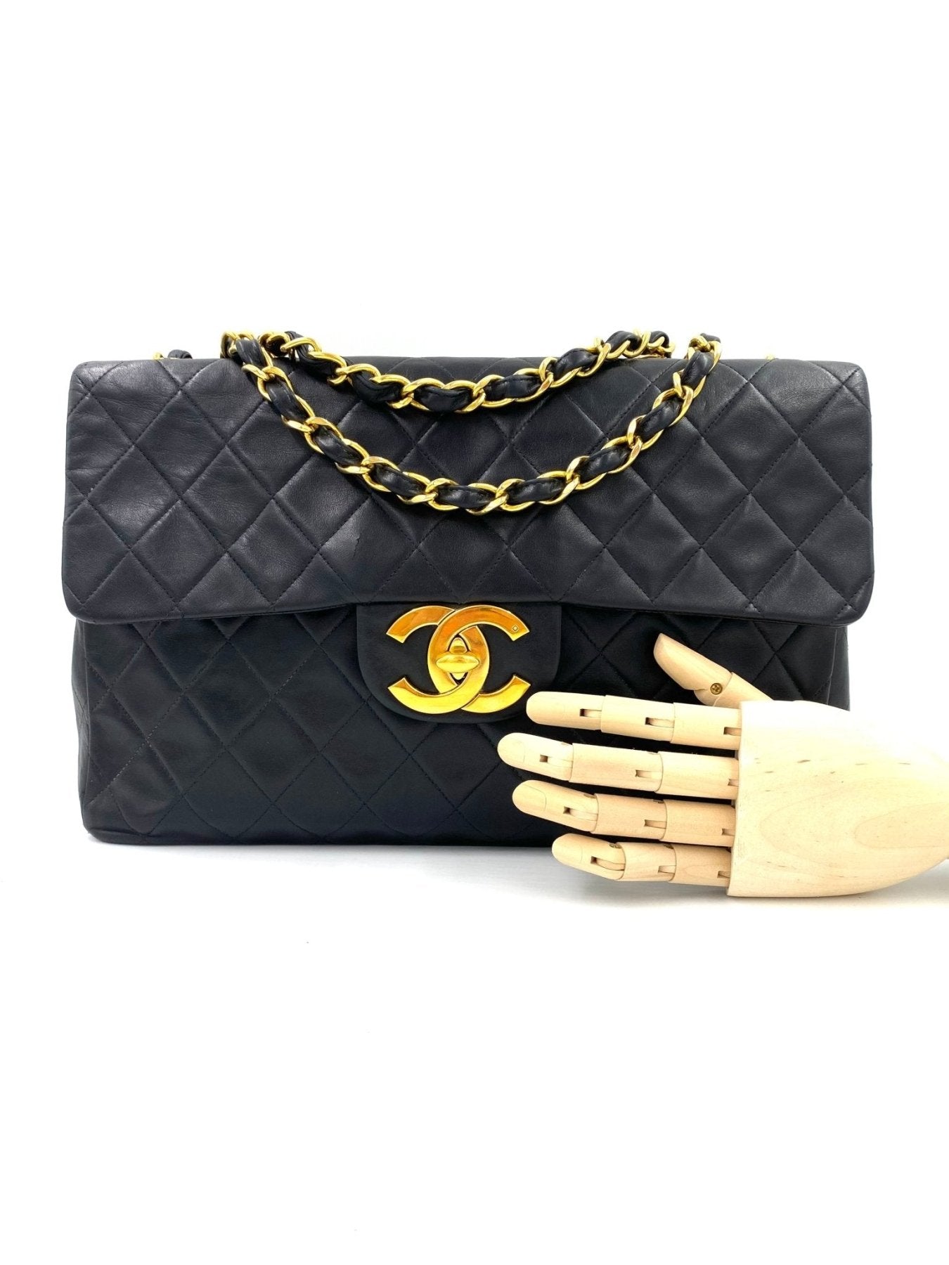 CHANEL Timeless Single Flap Bag Maxi schwarz mit gestepptem Lammleder und goldfarbener Kette auf weissem Hintergrund