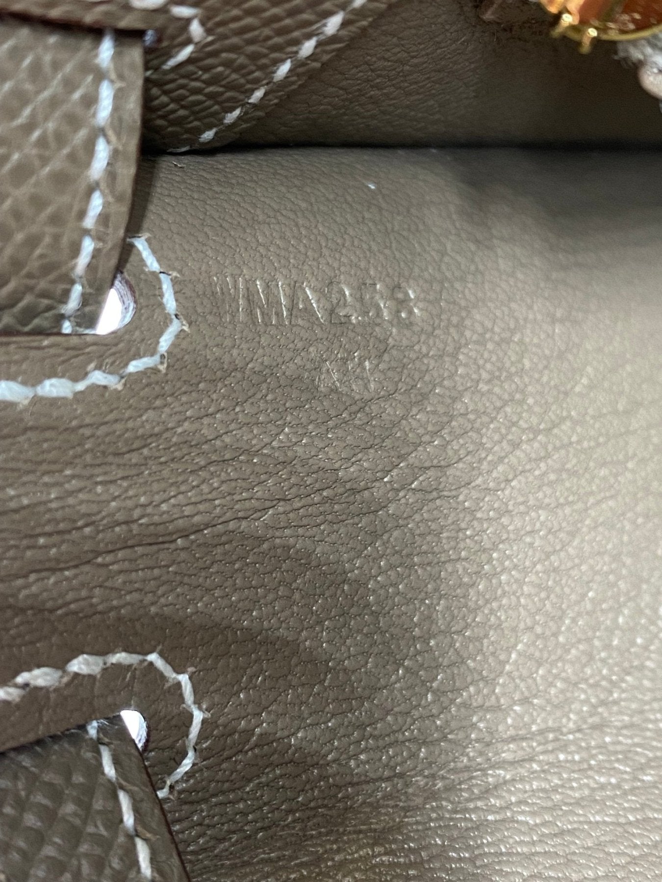 Nahaufnahme des Hermes Stempels auf grauem Epsom Leder der Kelly 25 Tasche mit kontrastierender weisser Naht