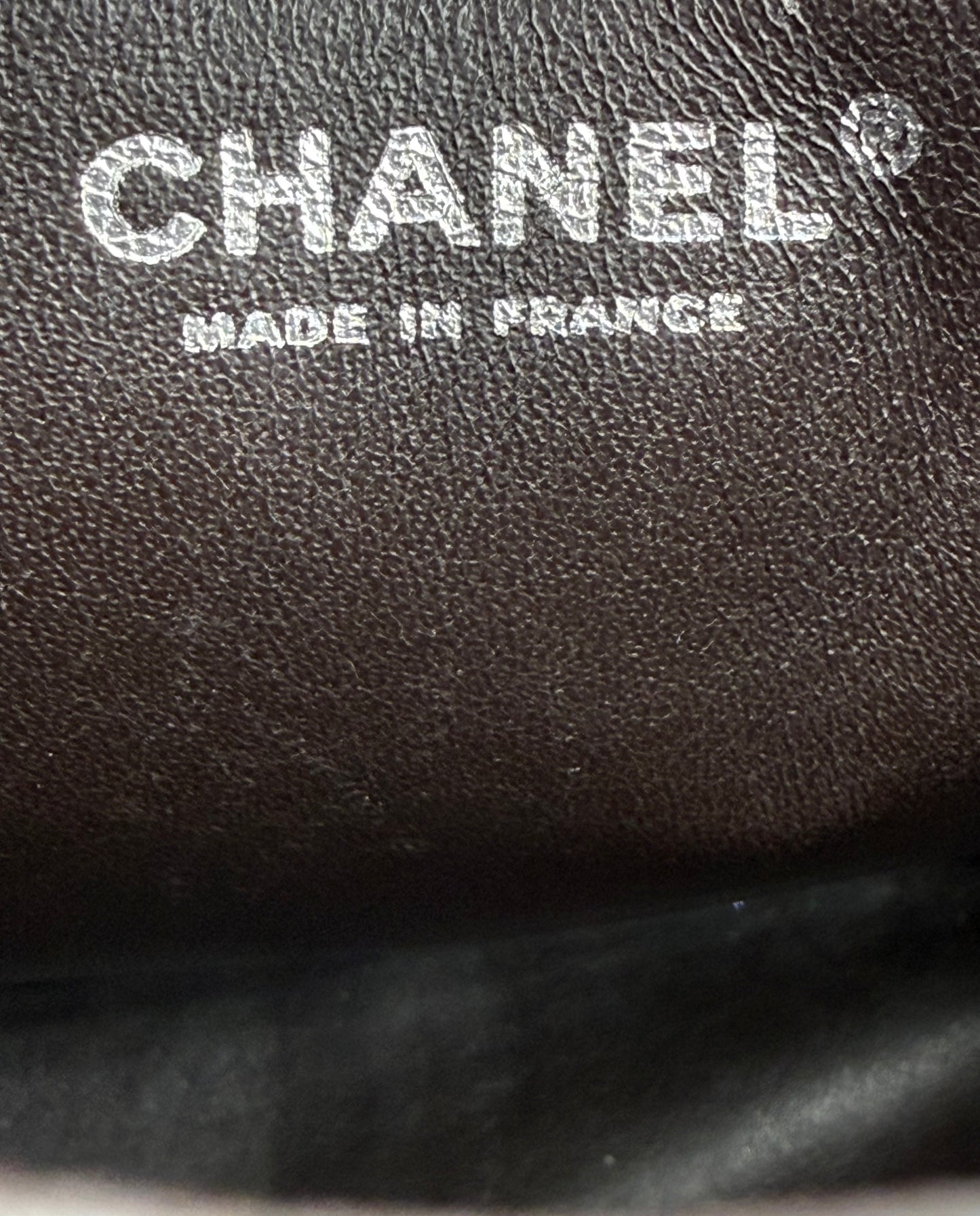 CHANEL Timeless Single Flap Jumbo Caviar dunkelbraun SHW Logo mit Prägung "Made in France" auf Lederoberfläche.