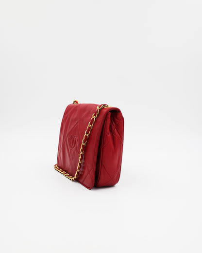 Rote gesteppte Chanel Schultertasche mit goldfarbener Kette vor hellem Hintergrund