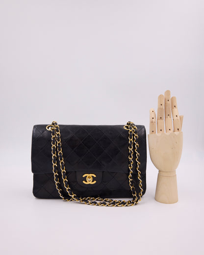 Schwarze gesteppte CHANEL-Handtasche mit goldener Kette neben einer hölzernen Handbüste