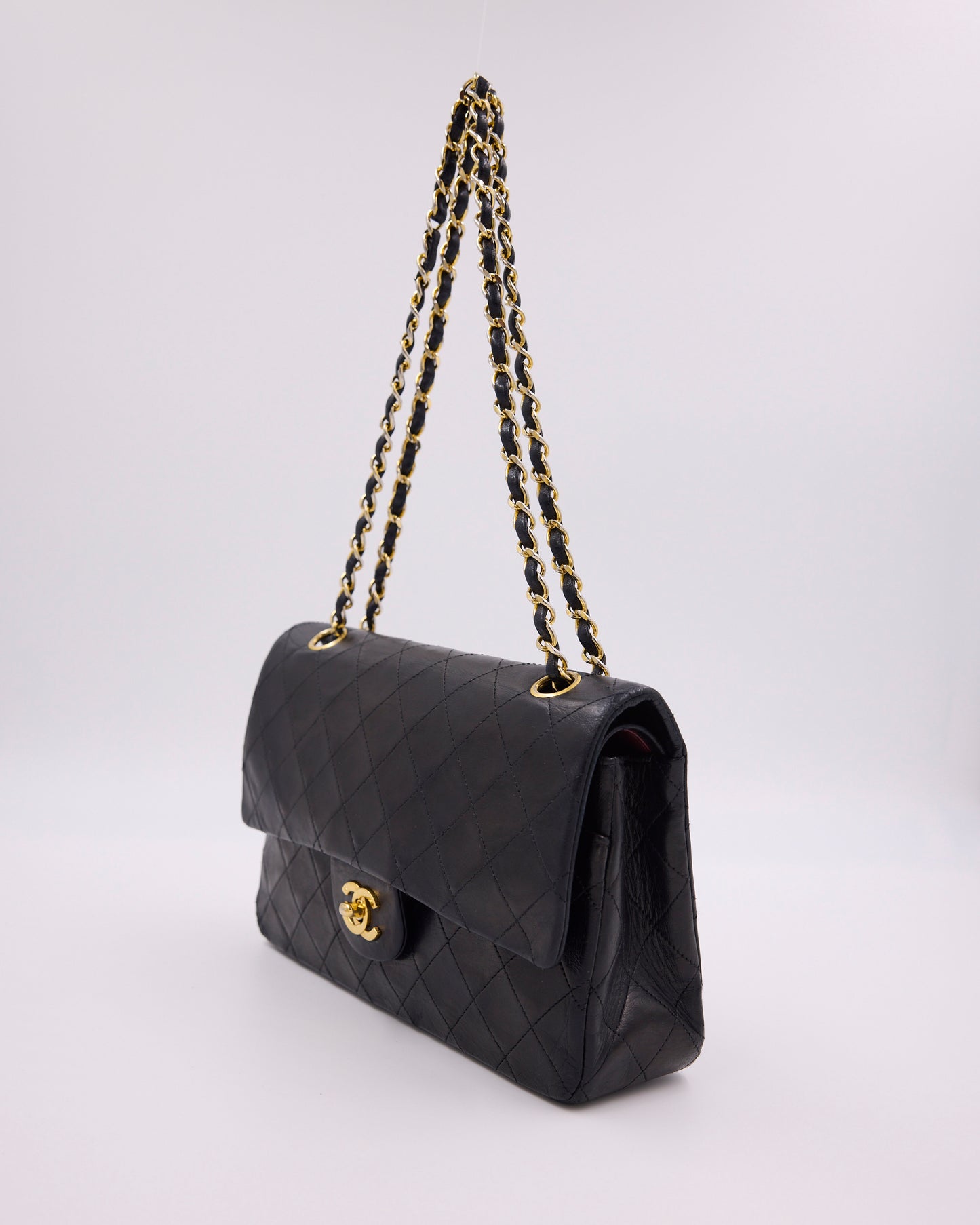 Schwarze gesteppte CHANEL Handtasche mit goldener Kette und CC-Verschluss vor hellem Hintergrund