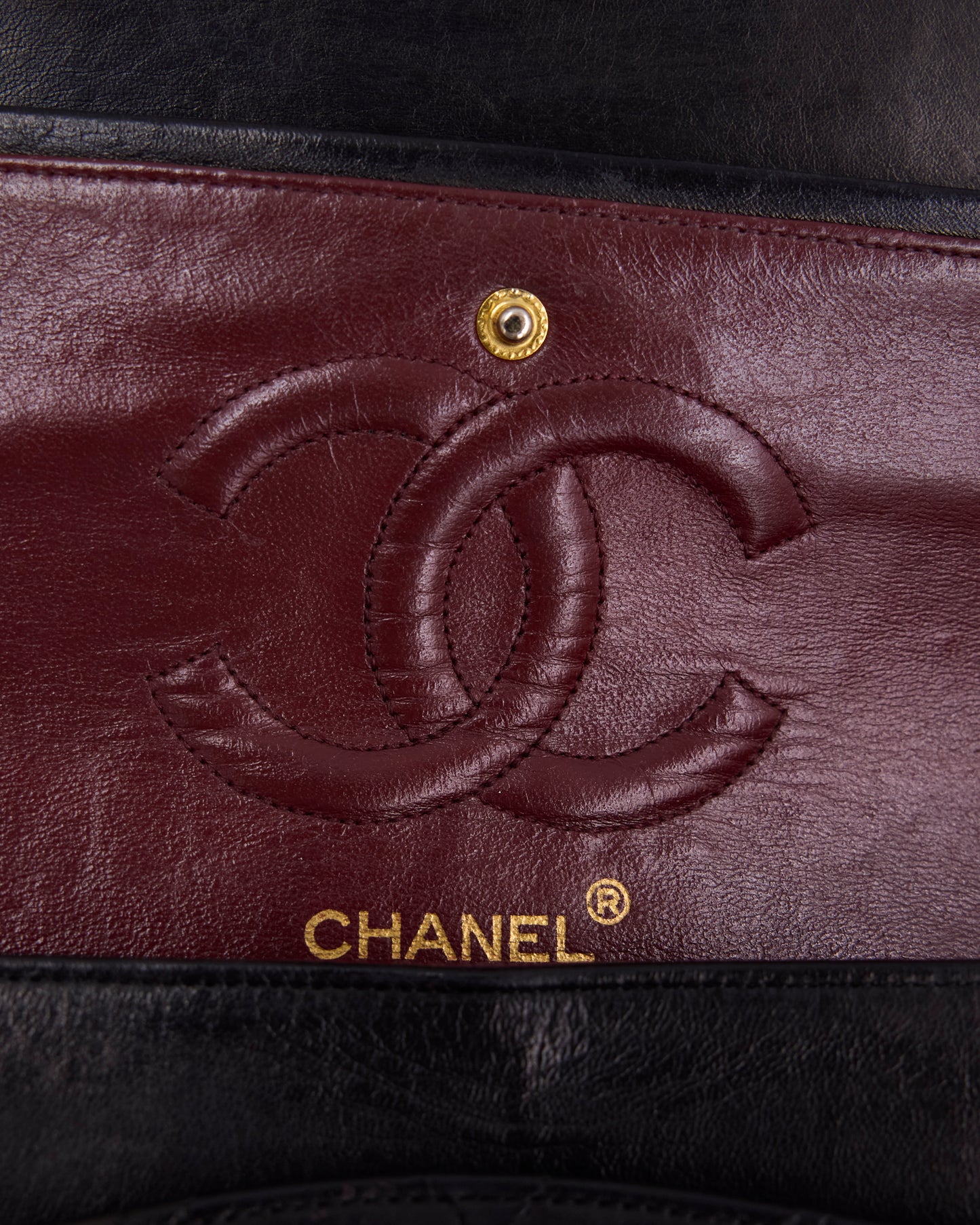 Nahaufnahme des Chanel Logos auf bordeauxrotem Leder mit goldfarbenem Druckknopf und schwarzem Rand