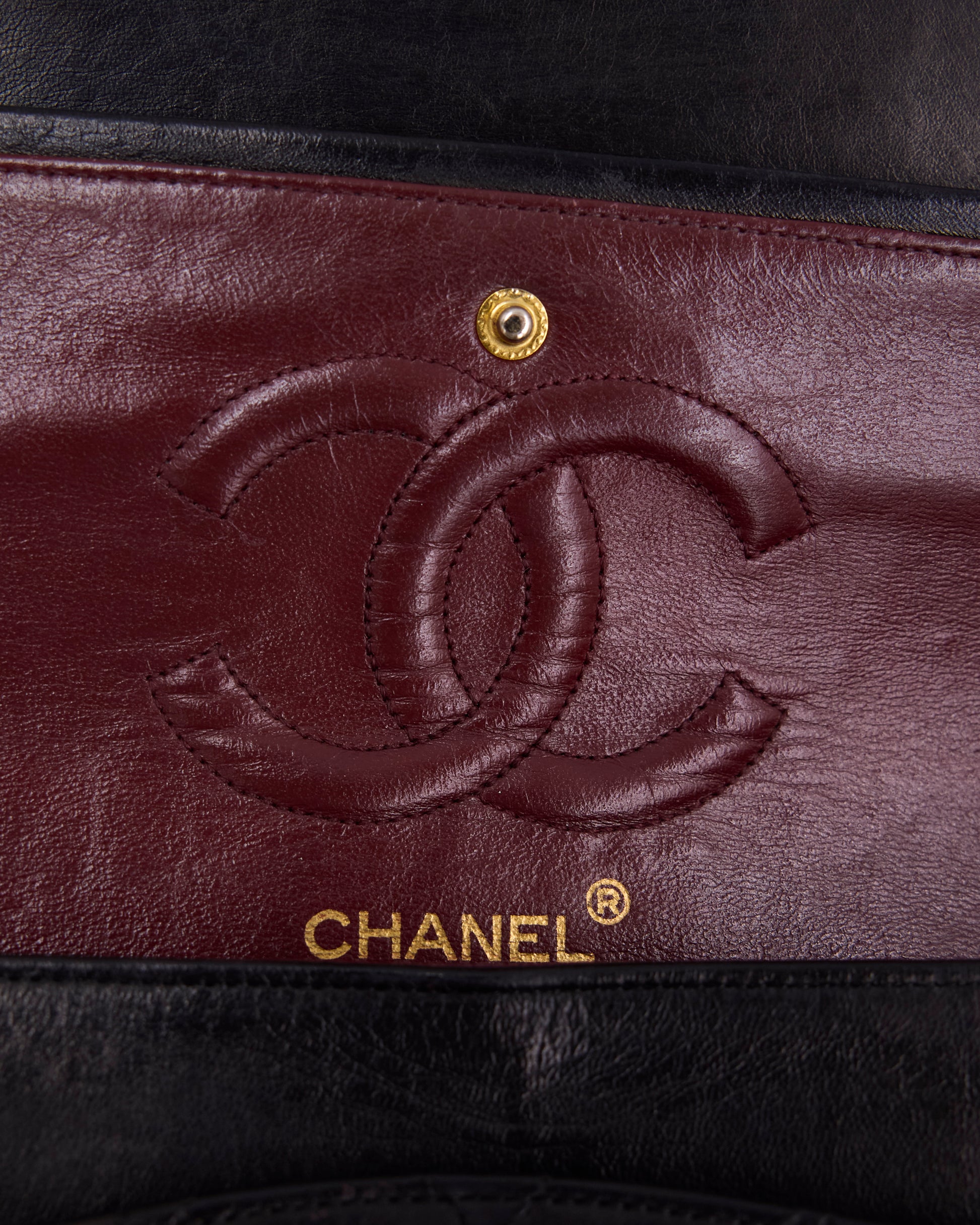 Nahaufnahme des Chanel Logos auf bordeauxrotem Leder mit goldfarbenem Druckknopf und schwarzem Rand