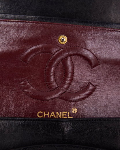 Nahaufnahme des Chanel Logos auf bordeauxrotem Leder mit goldfarbenem Druckknopf und schwarzem Rand