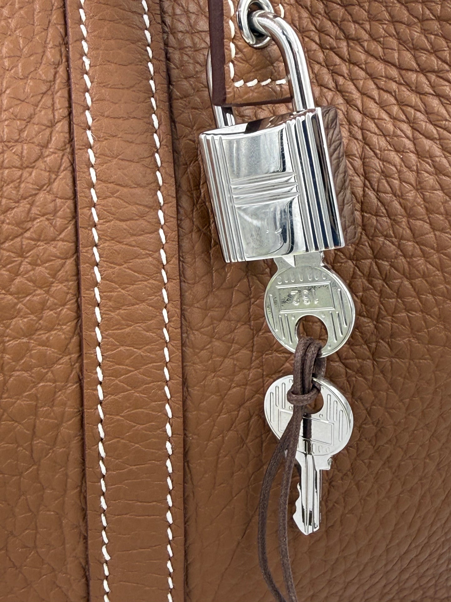Detailaufnahme des Schlosses und der Schlüssel an der HERMÈS Picotin 26 Lock Clemence gold PHW Tasche aus braunem Leder.
