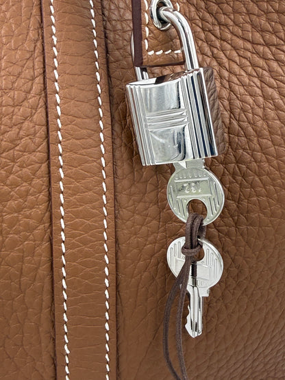 Detailaufnahme des Schlosses und der Schlüssel an der HERMÈS Picotin 26 Lock Clemence gold PHW Tasche aus braunem Leder.