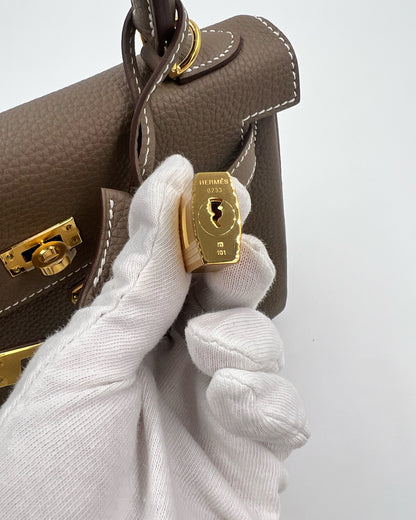 HERMÈS Kelly 25 Togo Etoupe GHW mit goldfarbenem Schloss und weißen Handschuhen