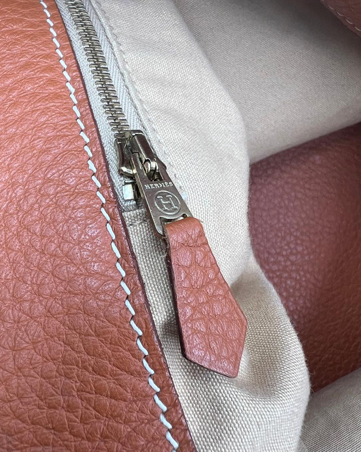 HERMÈS Thar GM Clemence Gold Detailansicht des Reißverschlusses mit Lederanhänger und hellem Innenfutter