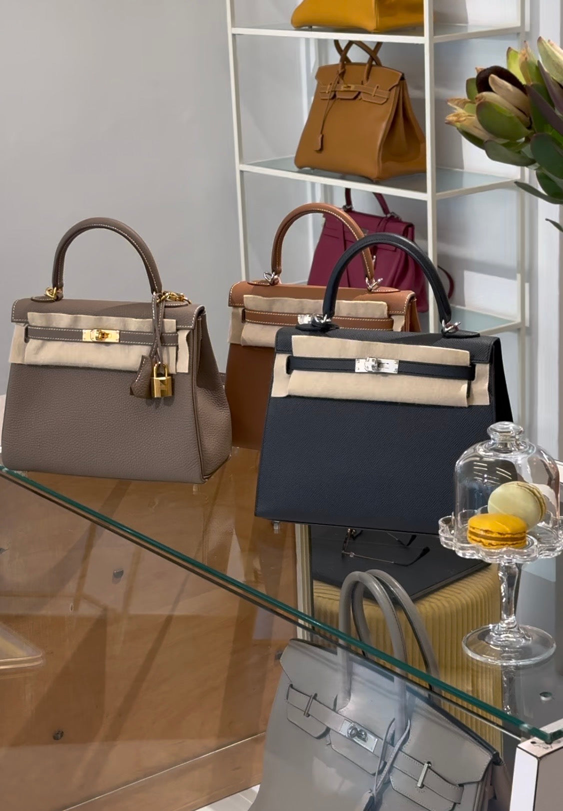 Mehrere elegante Designerhandtaschen in verschiedenen Farben auf einem Glastisch und weißen Regal