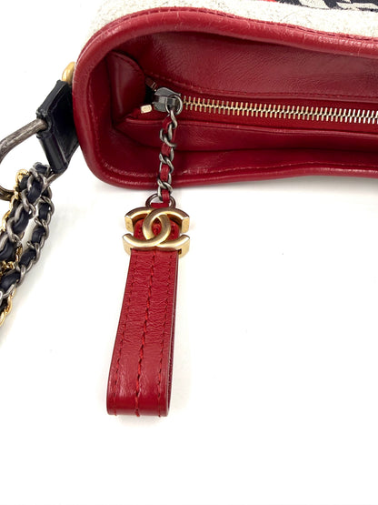 CHANEL Gabrielle medium dunkelblau Detailaufnahme des roten Leder-Reißverschlussanhängers mit goldfarbenem Logo und Kettenriemen