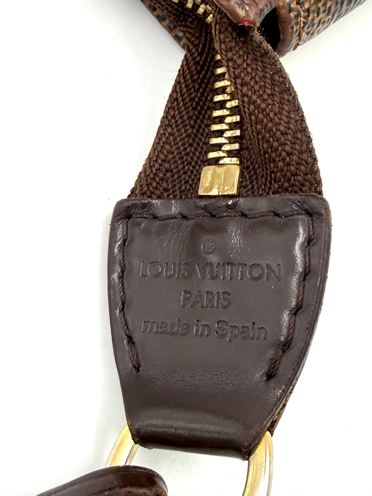 Nahe Aufnahme des Lederlabels mit Prägung von LOUIS VUITTON Pochette Accessoires Damier Ebene aus braunem Canvas und Leder.