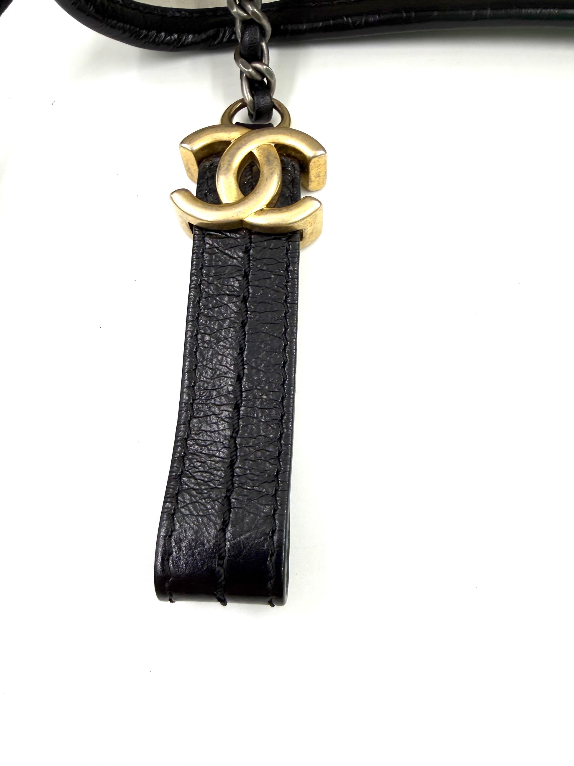 CHANEL Gabrielle small weiß/schwarz mit goldfarbenem Logo-Anhänger aus Leder und Metall in Nahaufnahme.