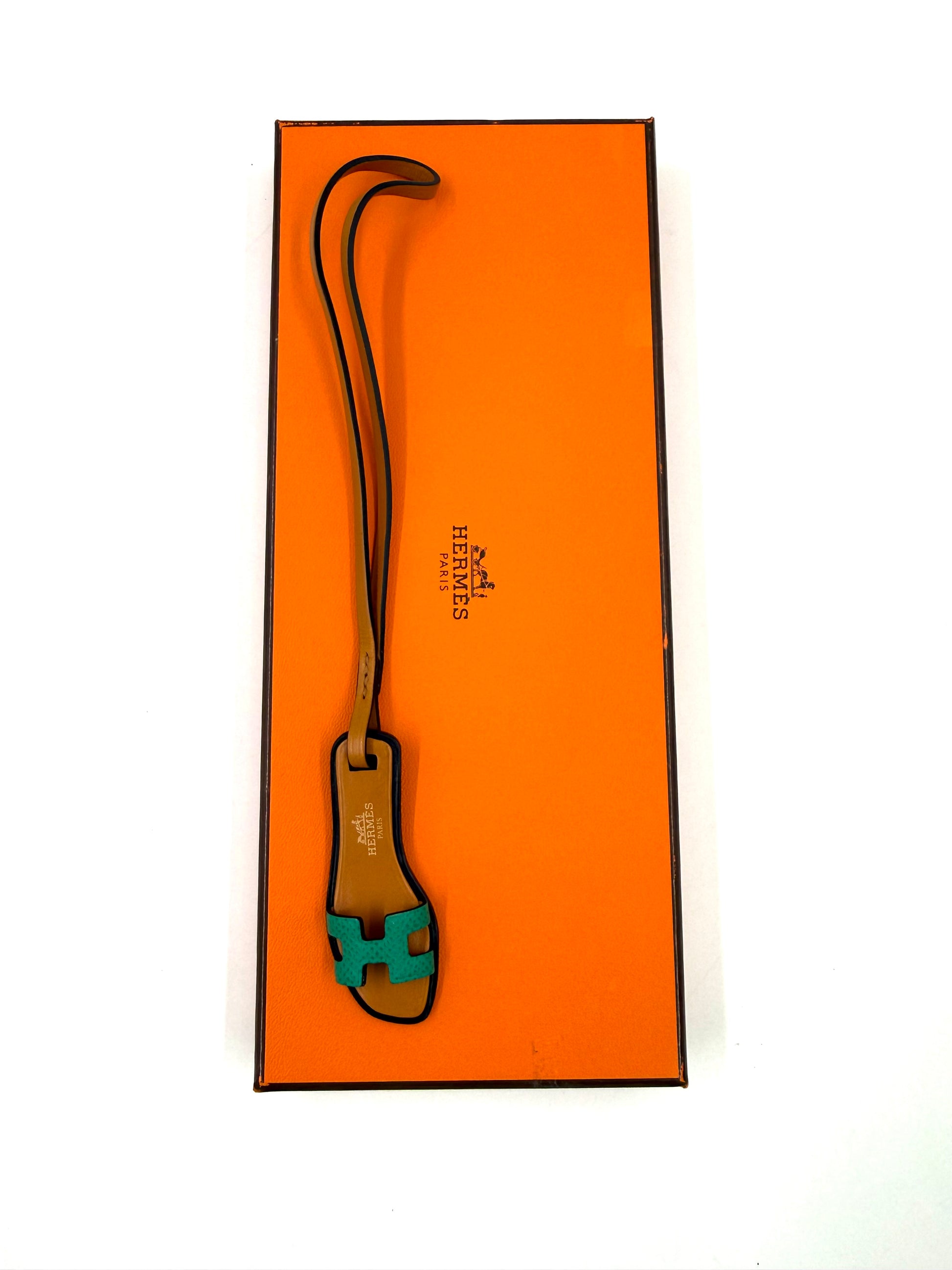 Hochwertiger HERMÈS Oran Nano Anhäger in Türkis und Braun auf ikonischer oranger Geschenkbox liegend.