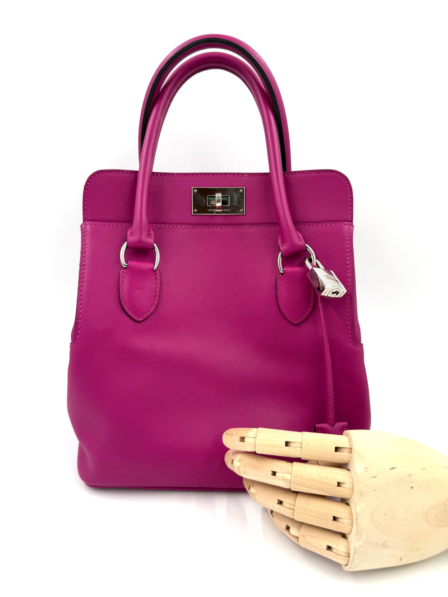 HERMÈS Toolbox 22 fuchsia PHW in kräftigem Pink mit silbernem Verschluss und eleganten Henkeln, präsentiert mit Holzmodellhand.