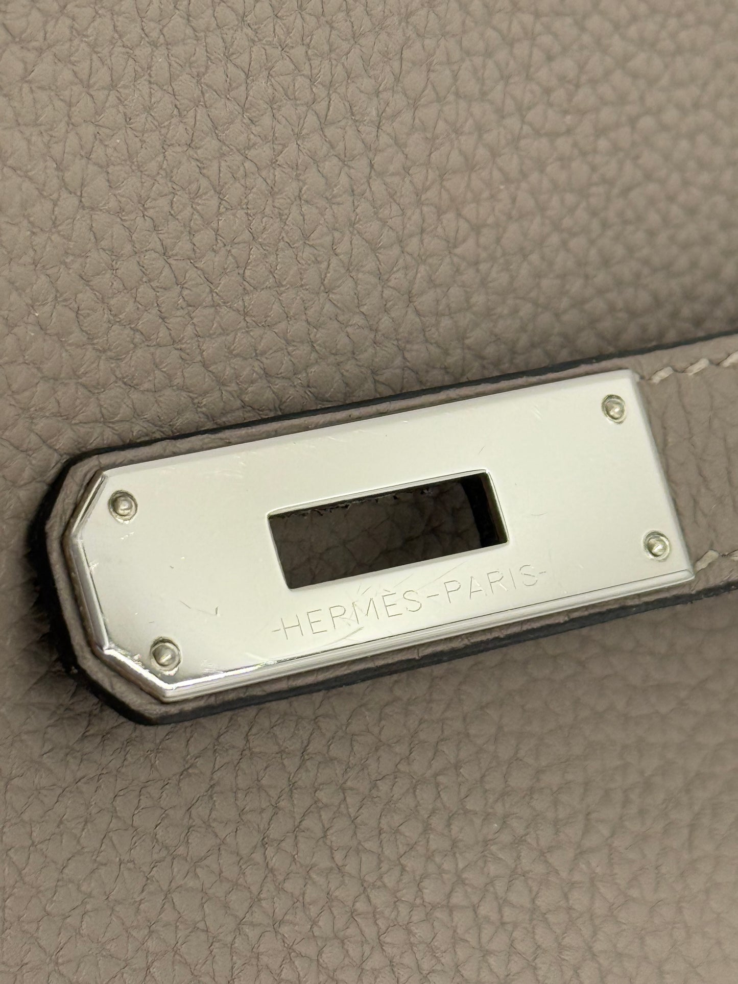 HERMÈS Kelly 32 Retourne Gris Asphalte PHW Detailansicht der palladiumfarbenen Verschlussplatte und grauem Clemence Leder.