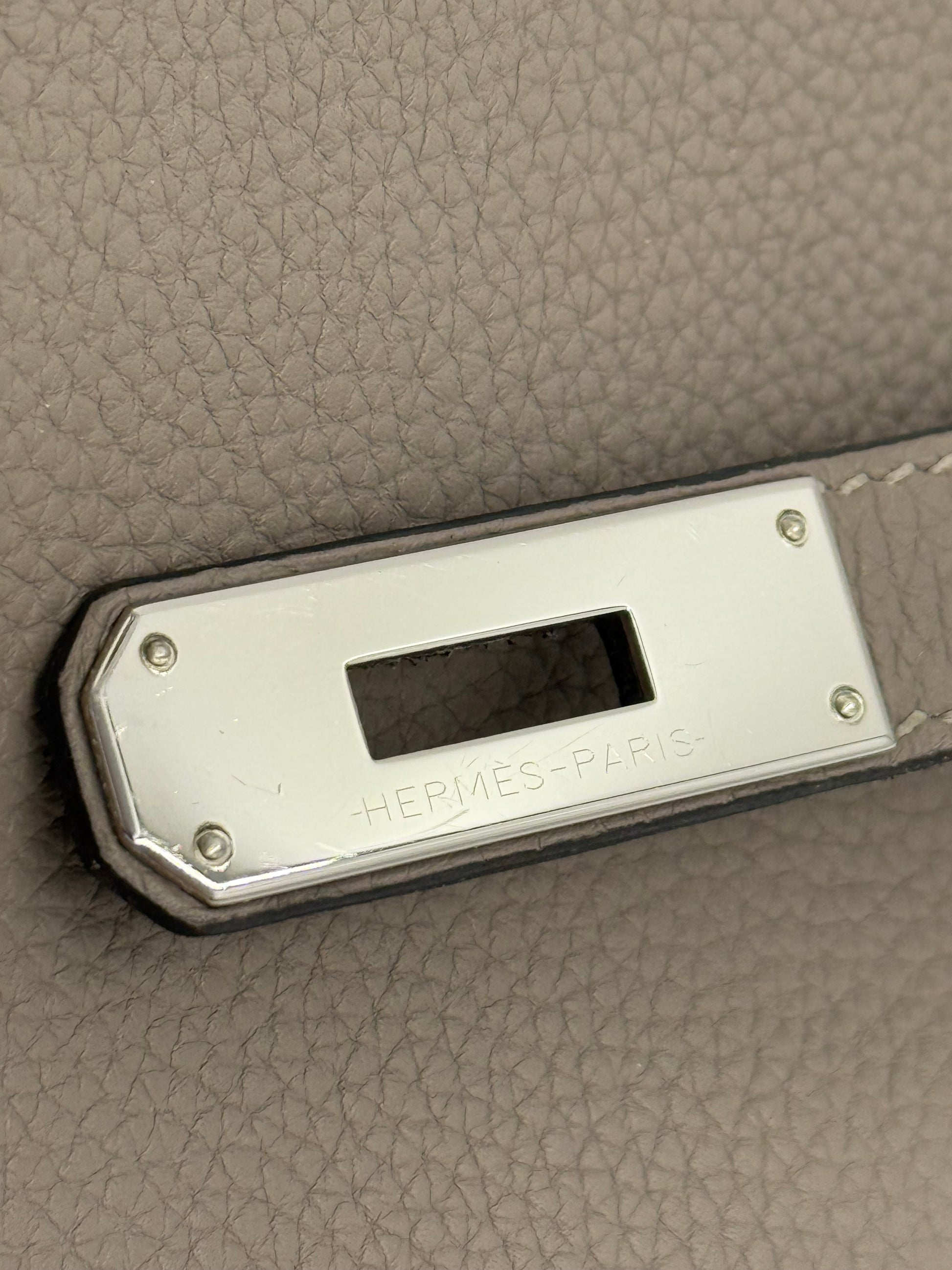 HERMÈS Kelly 32 Retourne Gris Asphalte PHW Detailansicht der palladiumfarbenen Verschlussplatte und grauem Clemence Leder.