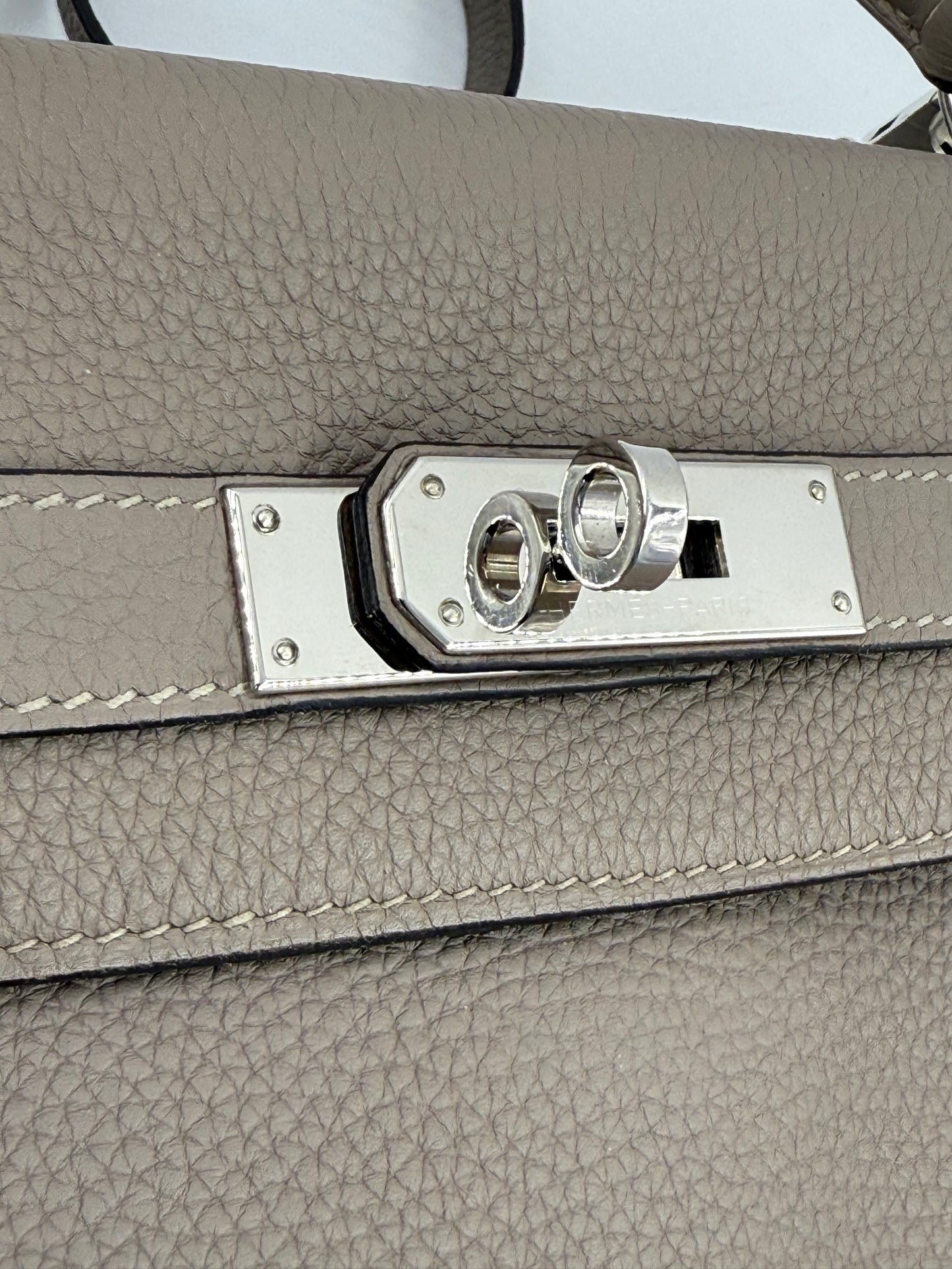 HERMÈS Kelly 32 Retourne Gris Asphalte PHW Detailansicht des Palladium-Verschlusses auf grauem Clemence-Leder.