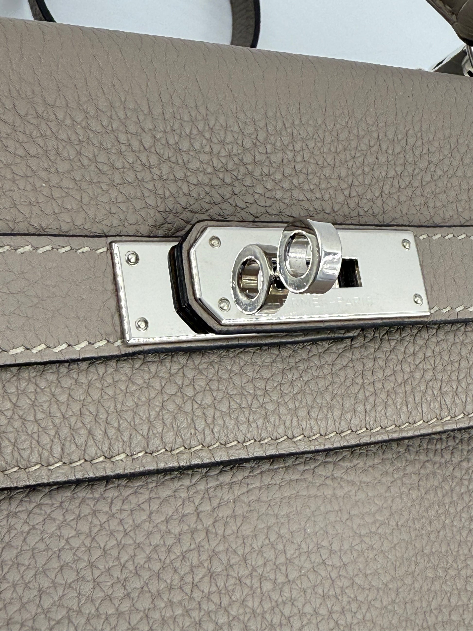 HERMÈS Kelly 32 Retourne Gris Asphalte PHW Detailansicht des Palladium-Verschlusses auf grauem Clemence-Leder.