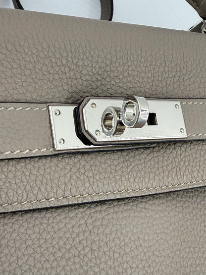 HERMÈS Kelly 32 Retourne Gris Asphalte PHW Detailansicht des Palladium-Verschlusses auf grauem Clemence-Leder.
