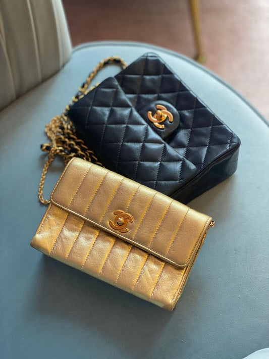 Beispielprodukt - Schwarze und goldene Designertaschen mit gestepptem Leder und Kettengurt auf hellblauem Stuhl