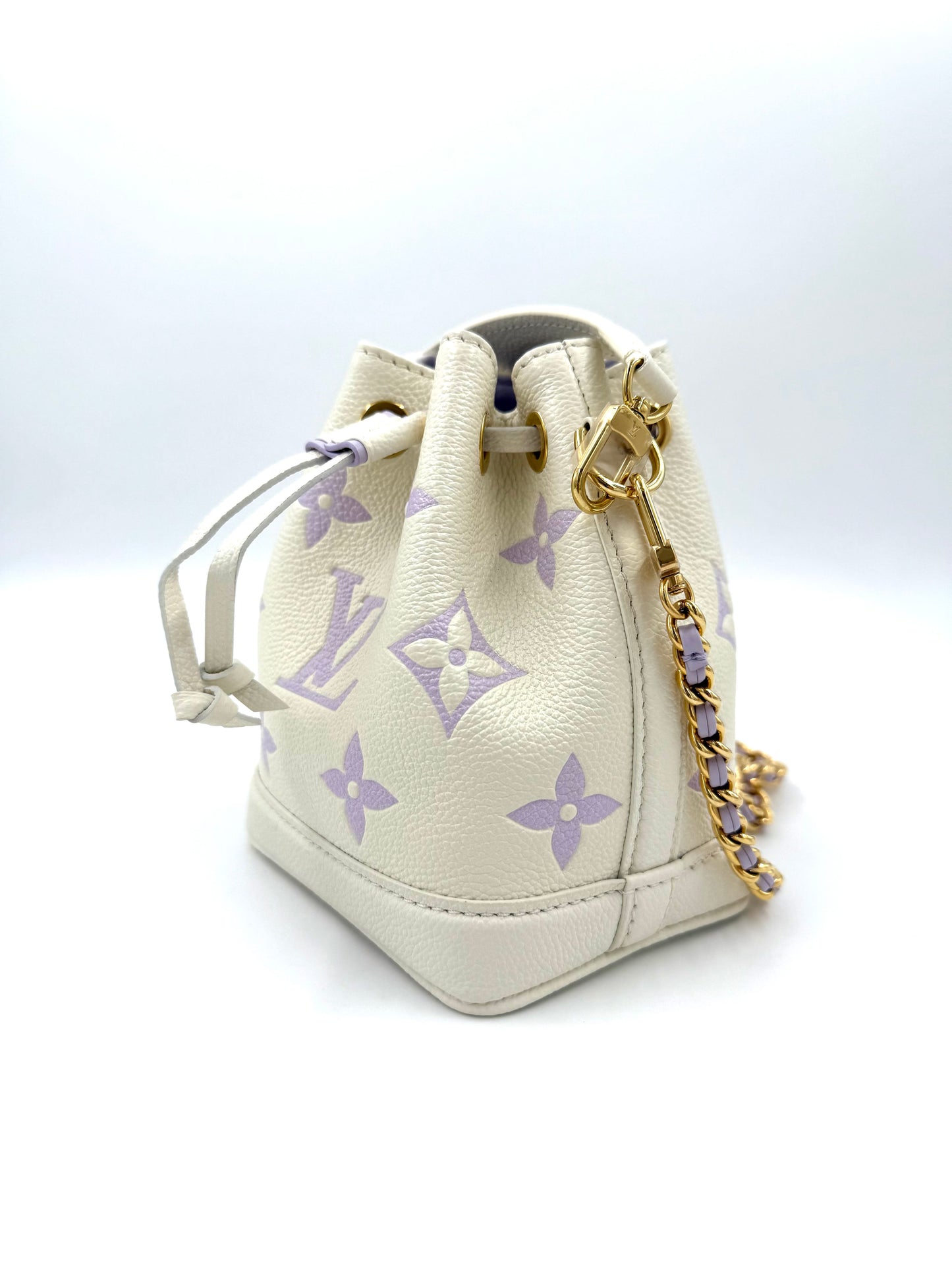 LOUIS VUITTON Nano Noe Monogram Empreinte Handtasche in Creme mit fliederfarbenen LV-Monogrammen und goldener Kette.
