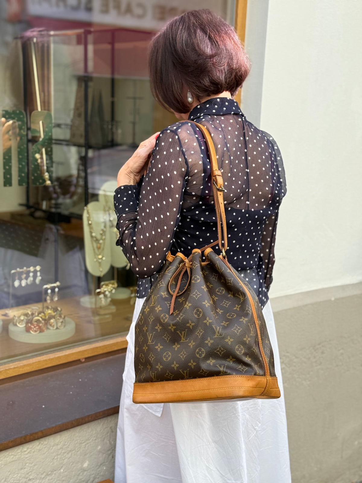 Frau mit brauner Louis Vuitton Monogramm-Tasche über der Schulter vor einem Schaufenster