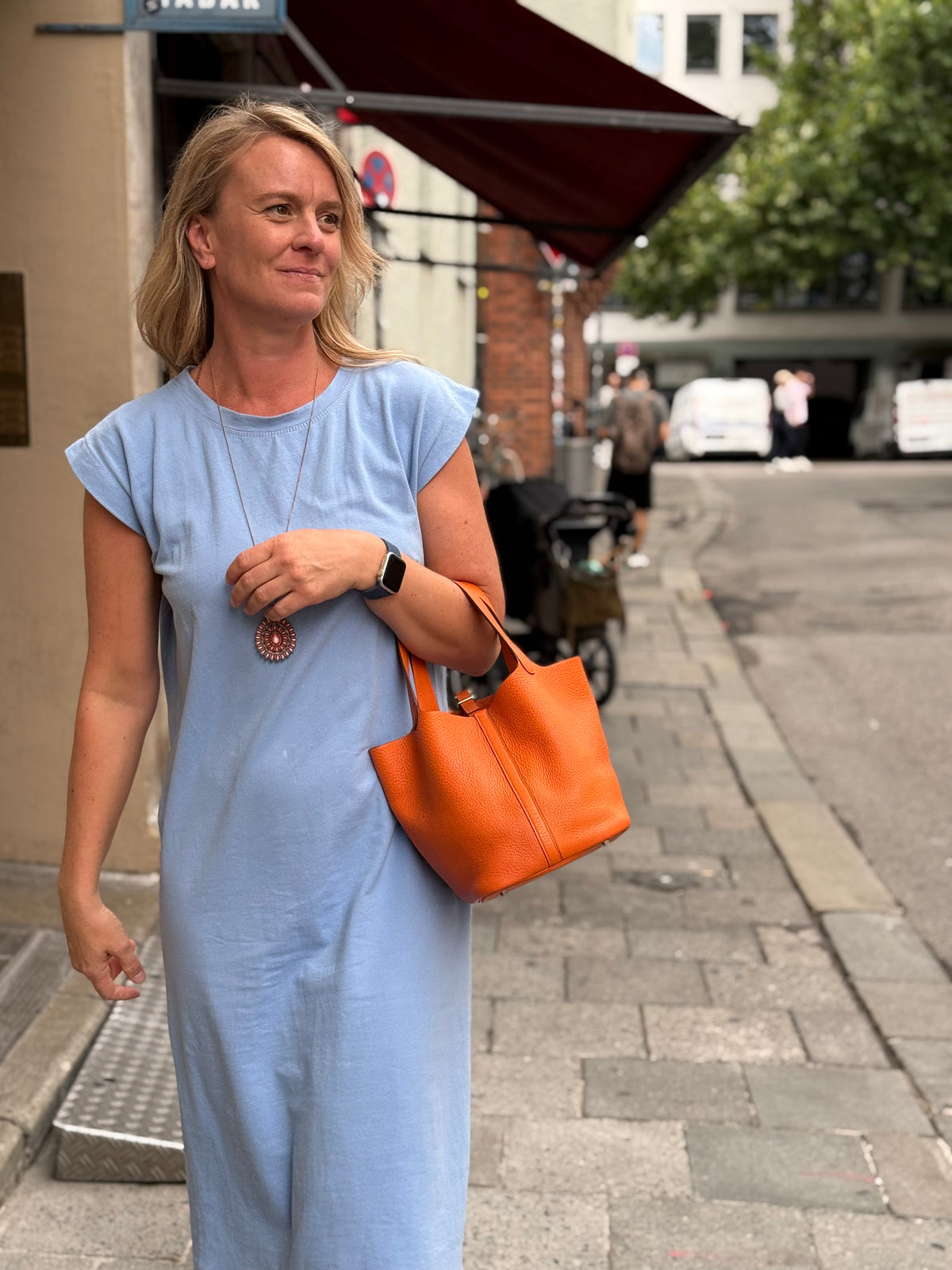 Frau in blauem Kleid mit orangefarbener Handtasche auf einer belebten Straße