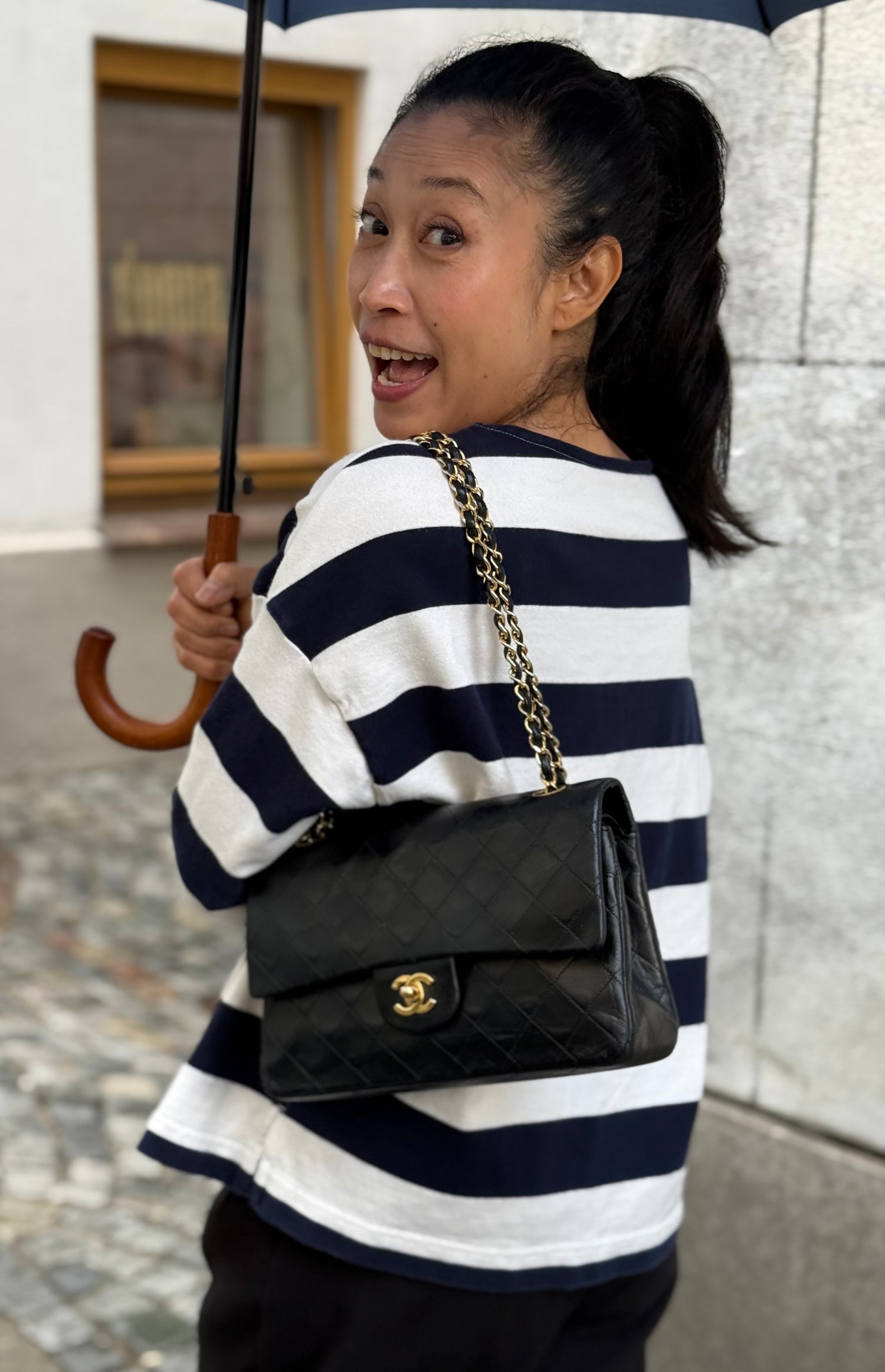 Frau mit gestreiftem Shirt und schwarzer gesteppter Chanel Schultertasche unter einem Regenschirm