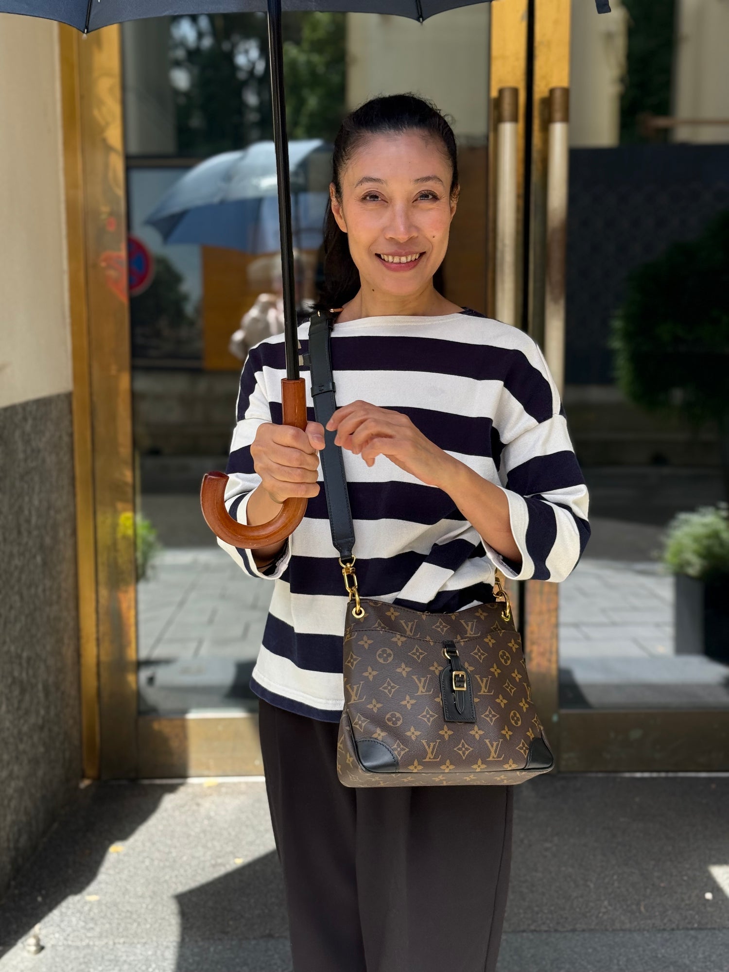 Frau mit Regenschirm und Louis Vuitton Monogramm-Umhängetasche vor einem Hauseingang