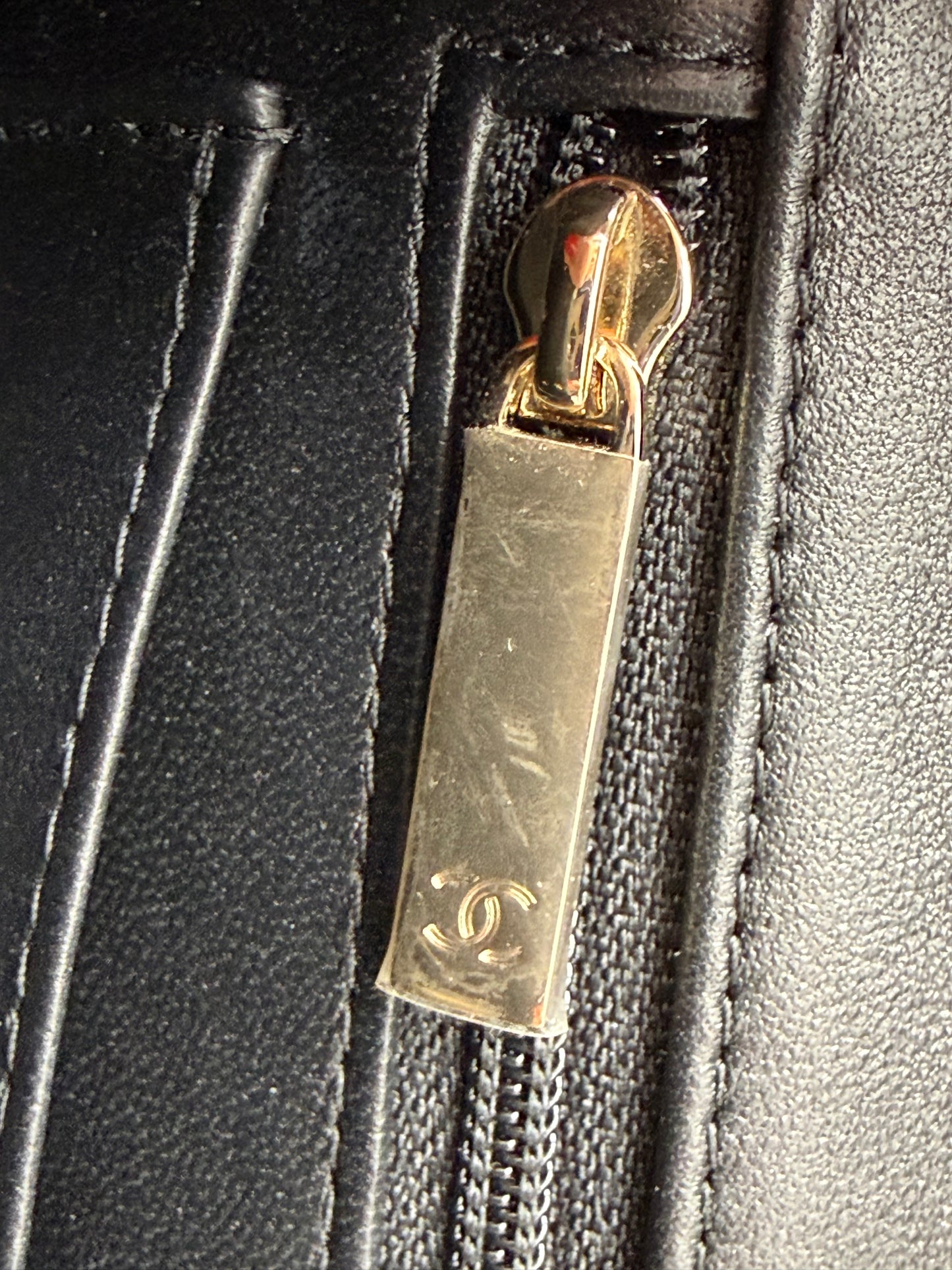 Detailaufnahme eines Reißverschlusses mit goldfarbenem Anhänger an der CHANEL Flap Bag Tweed schwarz/weiß GHW.