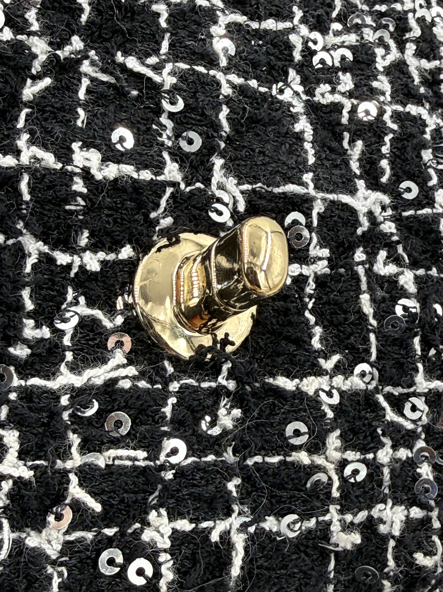 Detailaufnahme des goldfarbenen Verschlusses der CHANEL Flap Bag Tweed schwarz/weiß GHW mit Paillettenbesatz.