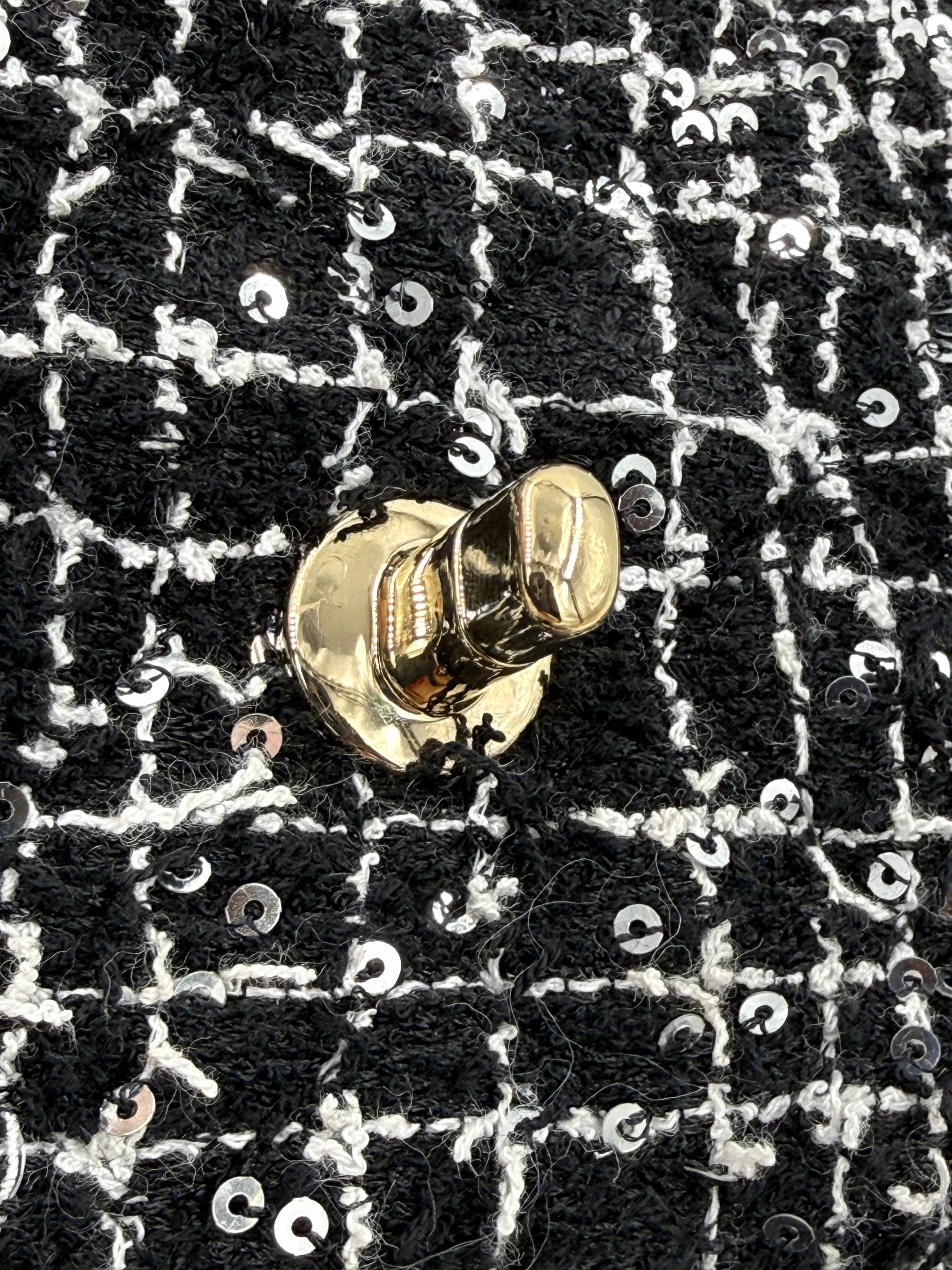 Detailaufnahme des goldfarbenen Verschlusses der CHANEL Flap Bag Tweed schwarz/weiß GHW mit Paillettenbesatz.