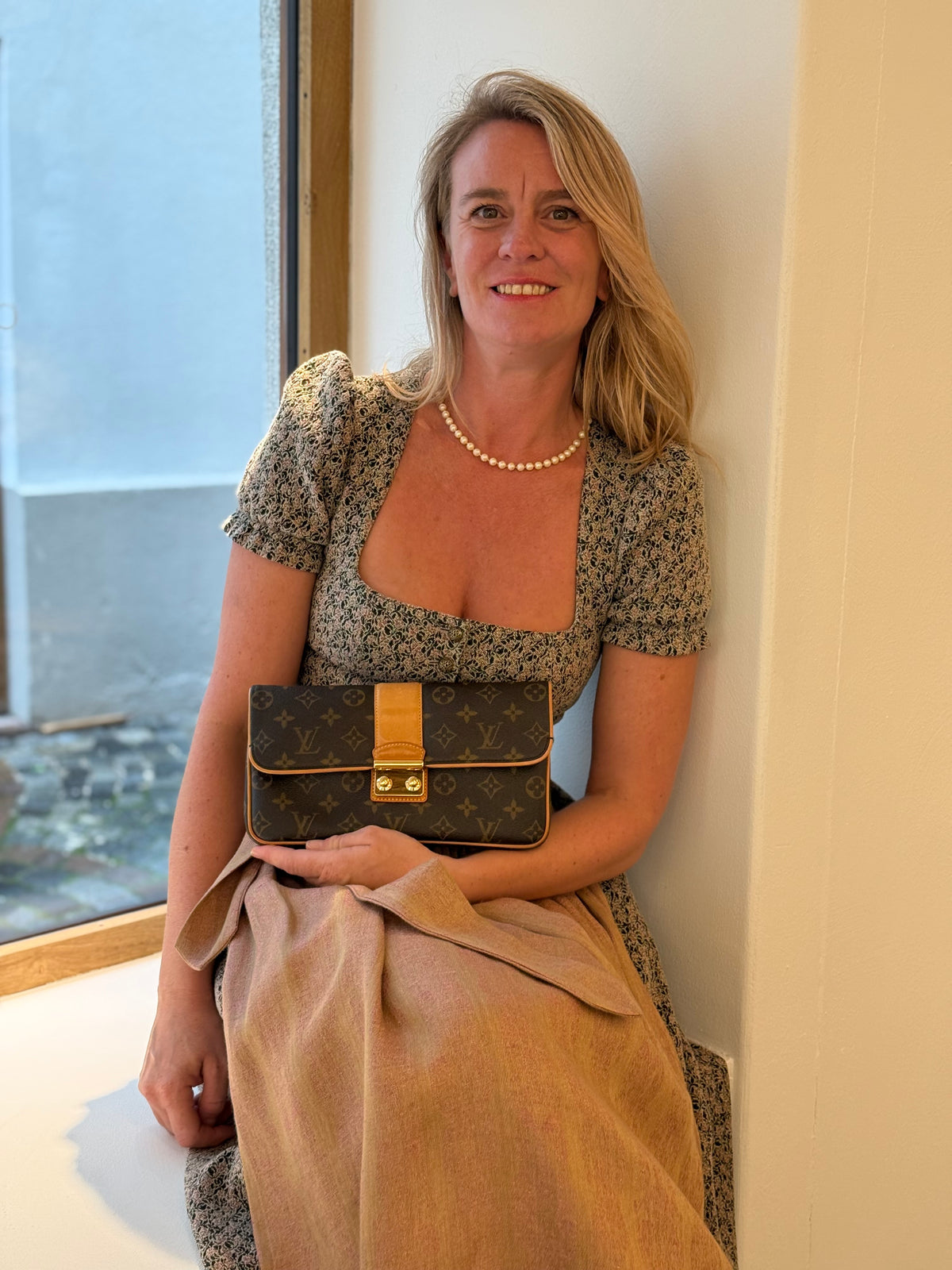 Frau im Kleid hält sitzend eine Louis Vuitton Monogram Clutch