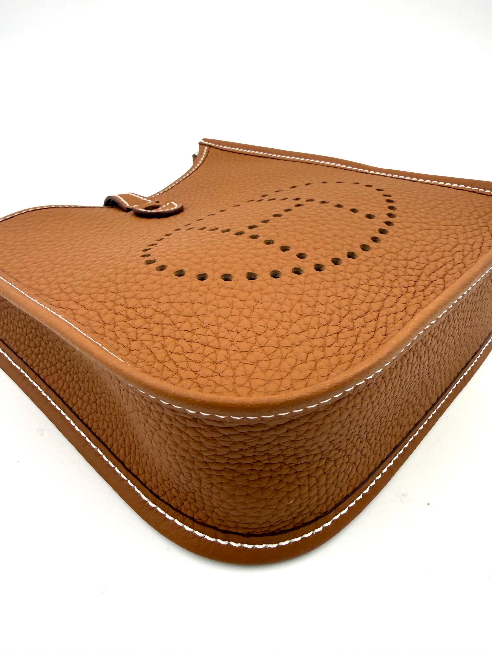 HERMÈS Evelyne 16 gold PHW aus genarbtem Leder mit sichtbaren weißen Nähten und perforiertem H-Logo in Nahaufnahme.