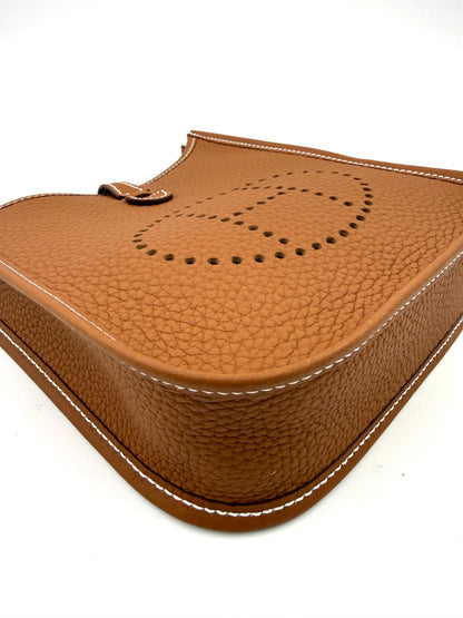 HERMÈS Evelyne 16 gold PHW aus genarbtem Leder mit sichtbaren weißen Nähten und perforiertem H-Logo in Nahaufnahme.