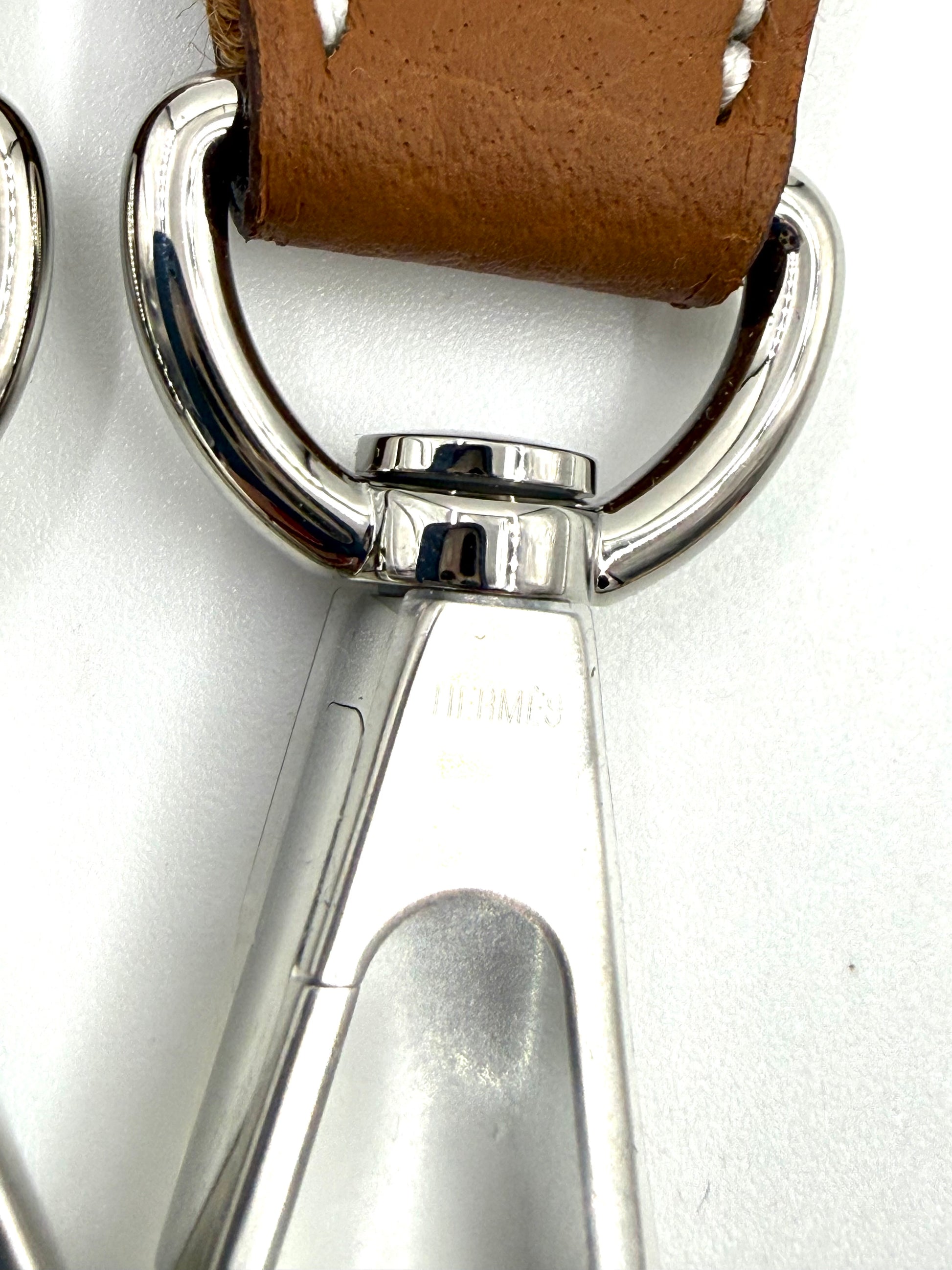 Detailaufnahme des metallischen Karabinerhakens und braunen Lederriemens der HERMÈS Evelyne 16 gold PHW Tasche.