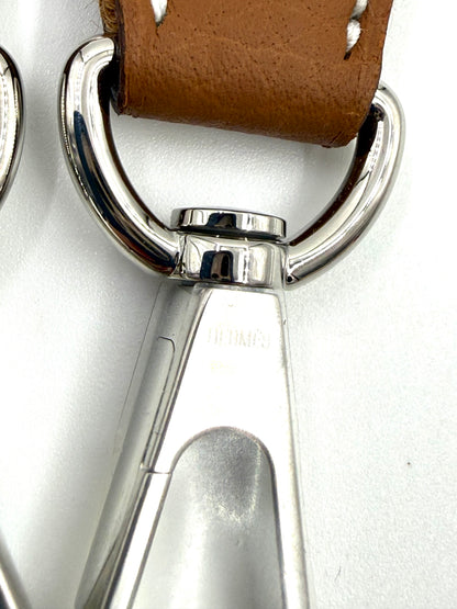 Detailaufnahme des metallischen Karabinerhakens und braunen Lederriemens der HERMÈS Evelyne 16 gold PHW Tasche.